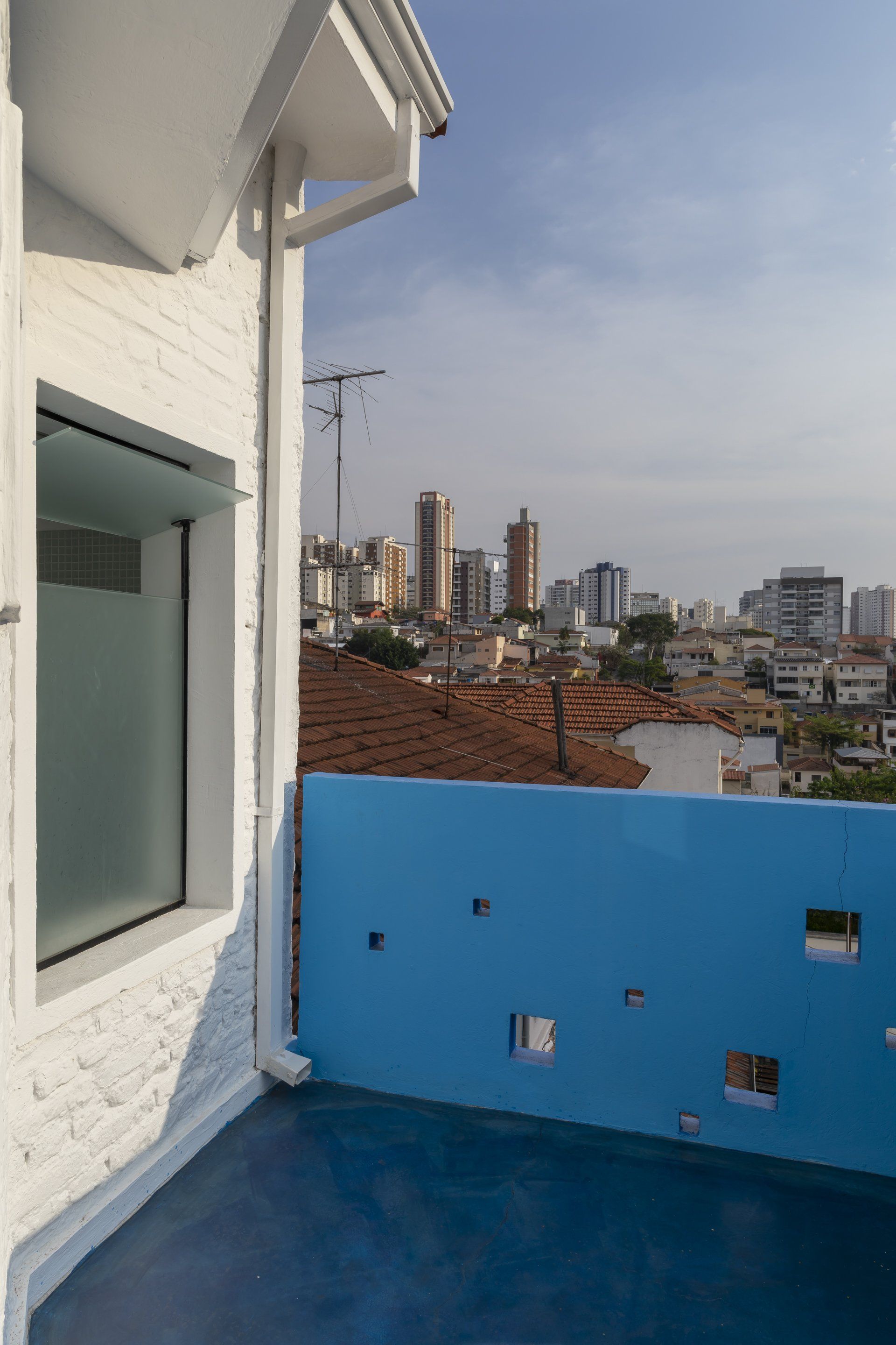 Uma varanda com uma cerca azul e uma janela com vista para a cidade.