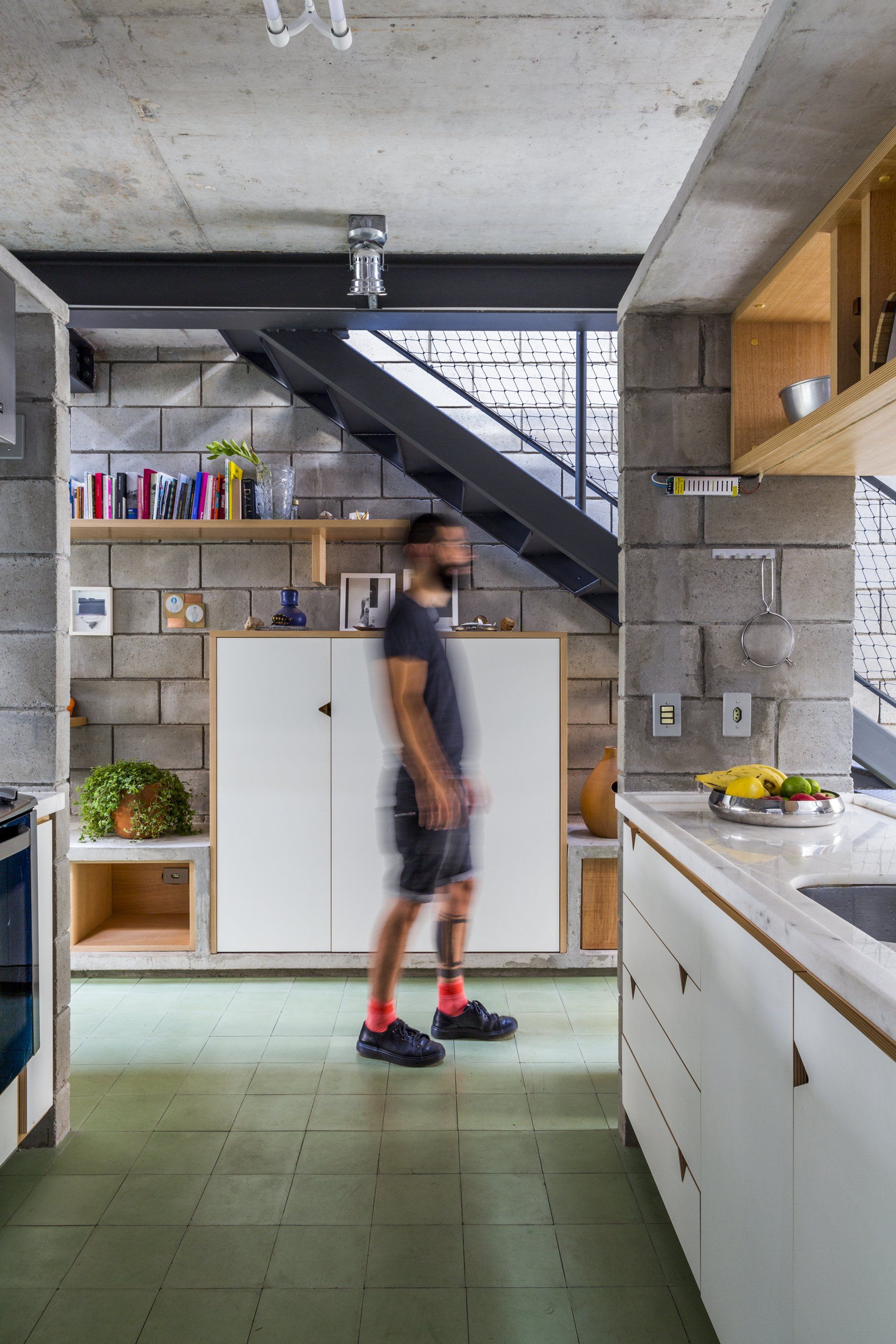 Um homem está andando em uma cozinha com uma escada ao fundo.