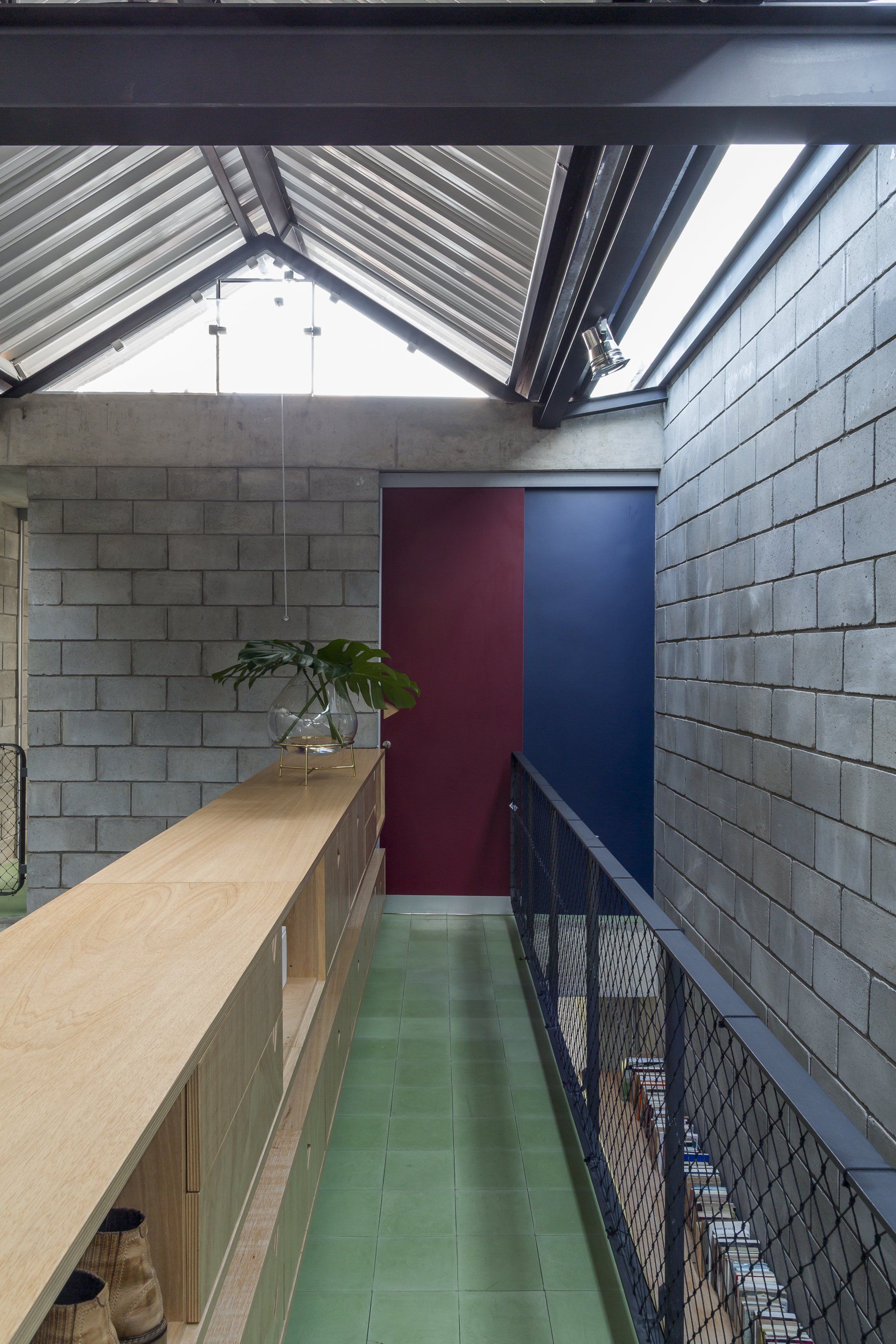 Um longo corredor com uma parede de tijolos e uma porta azul e vermelha.