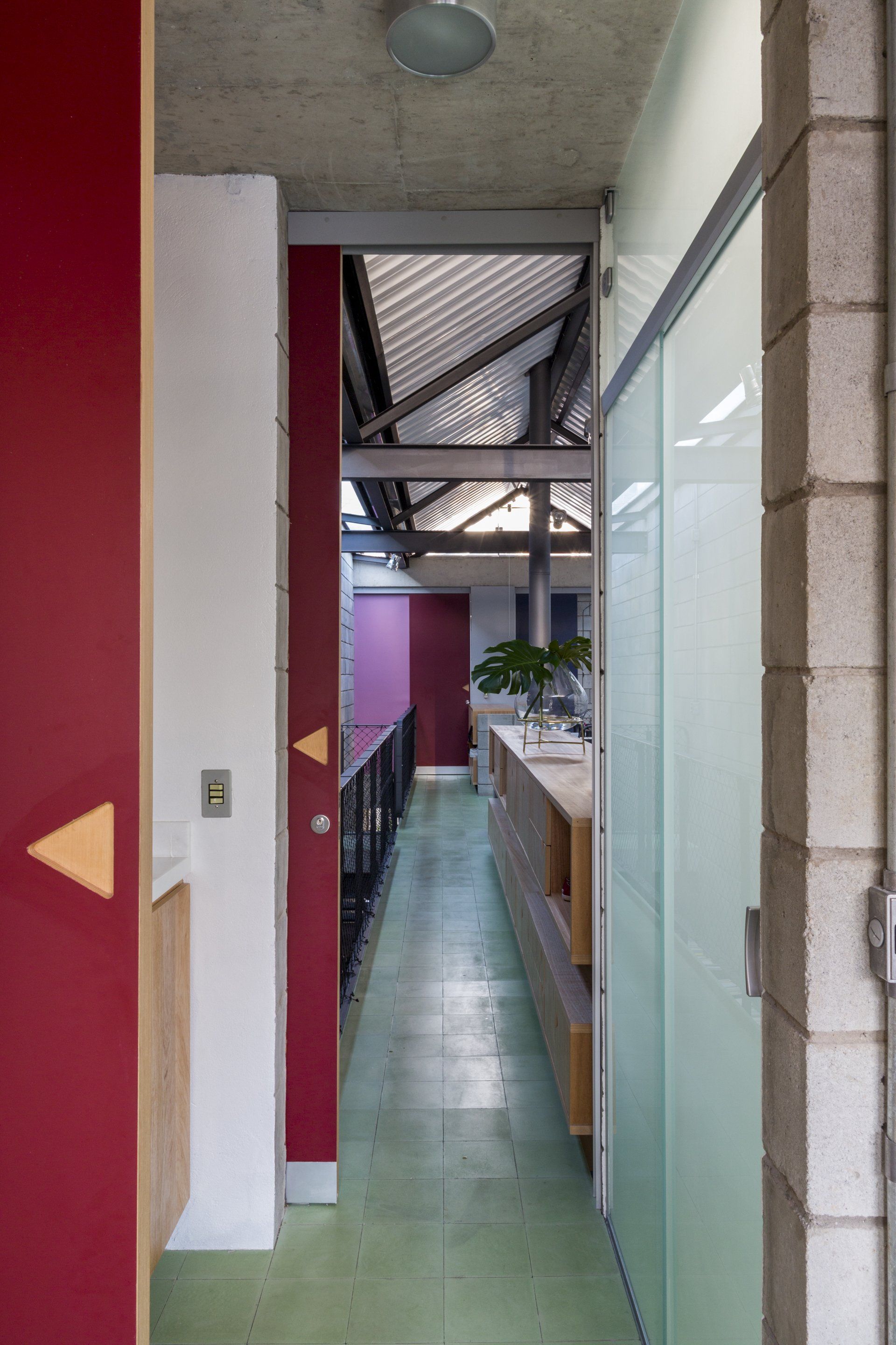 Um corredor de um prédio com porta vermelha e piso verde.