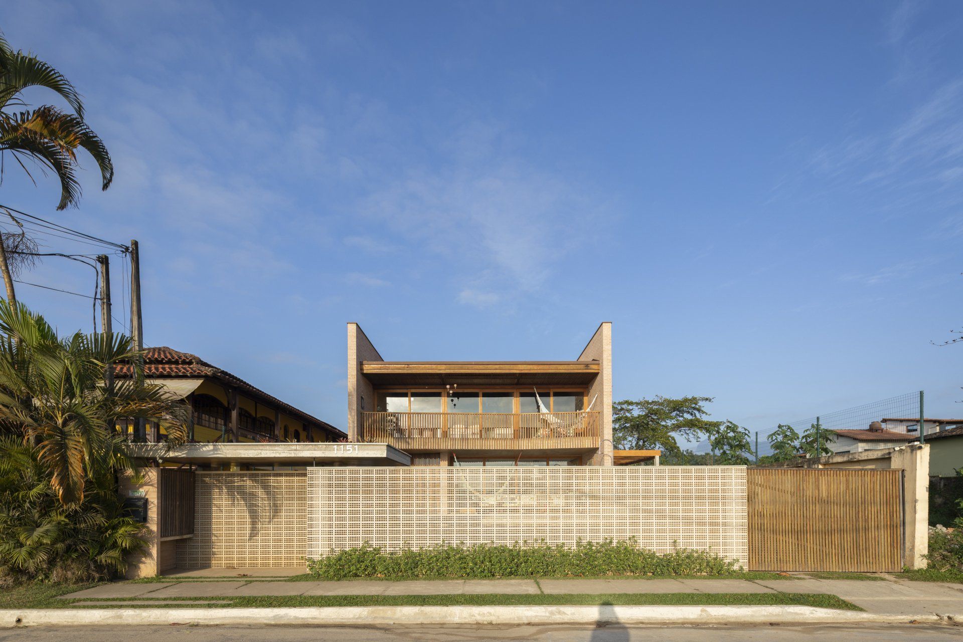 A frente de uma casa com uma cerca de madeira e um céu azul ao fundo.