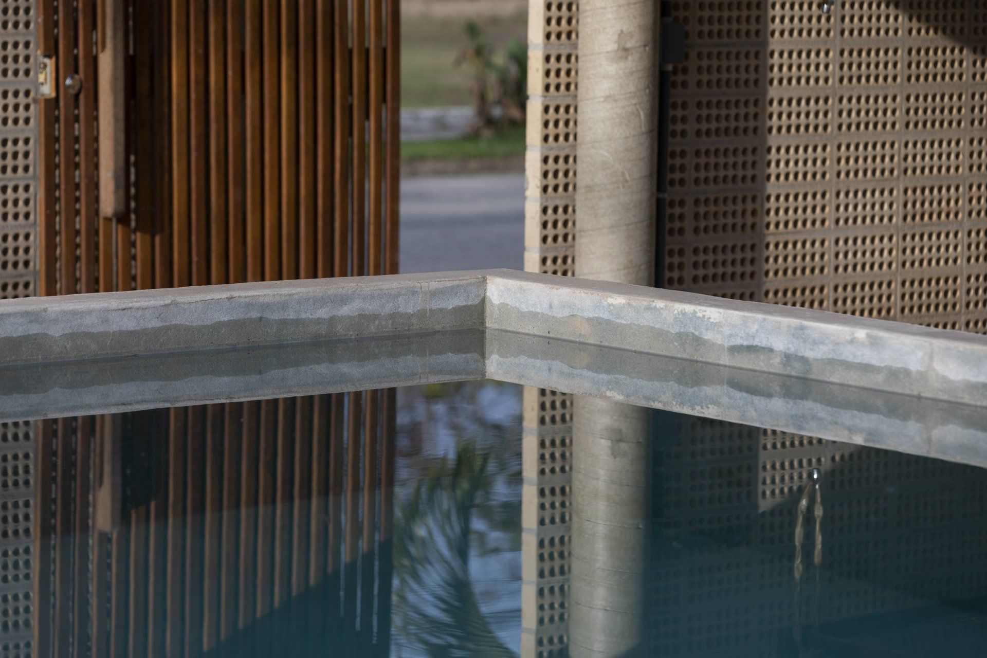 Uma piscina com uma cerca de madeira ao fundo e o reflexo de um prédio na água.