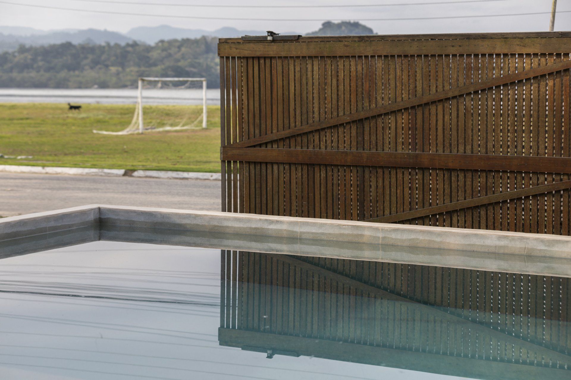 Uma piscina cercada por uma cerca de madeira e um gol de futebol ao fundo.