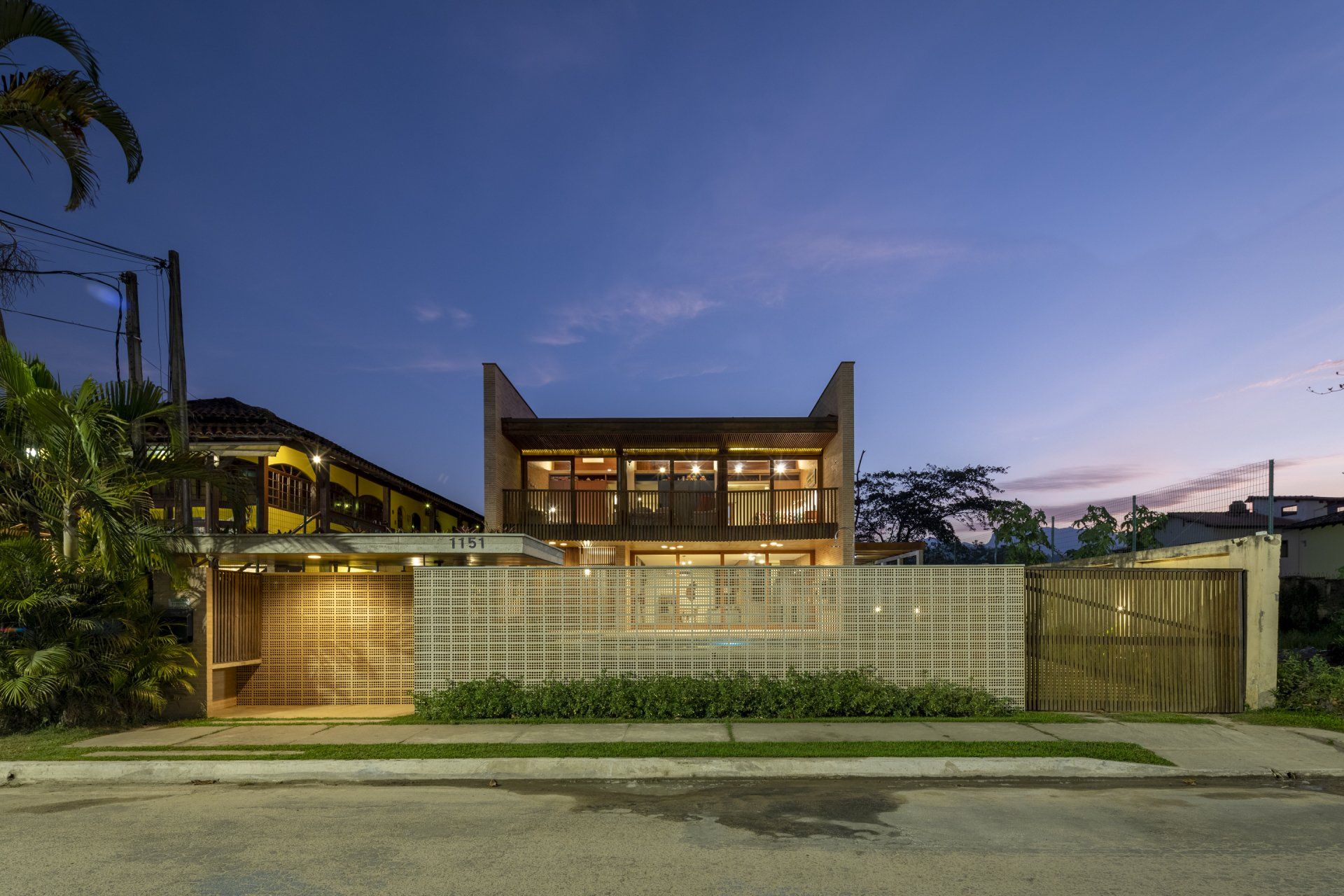 Uma grande casa com uma cerca na frente fica iluminada à noite.