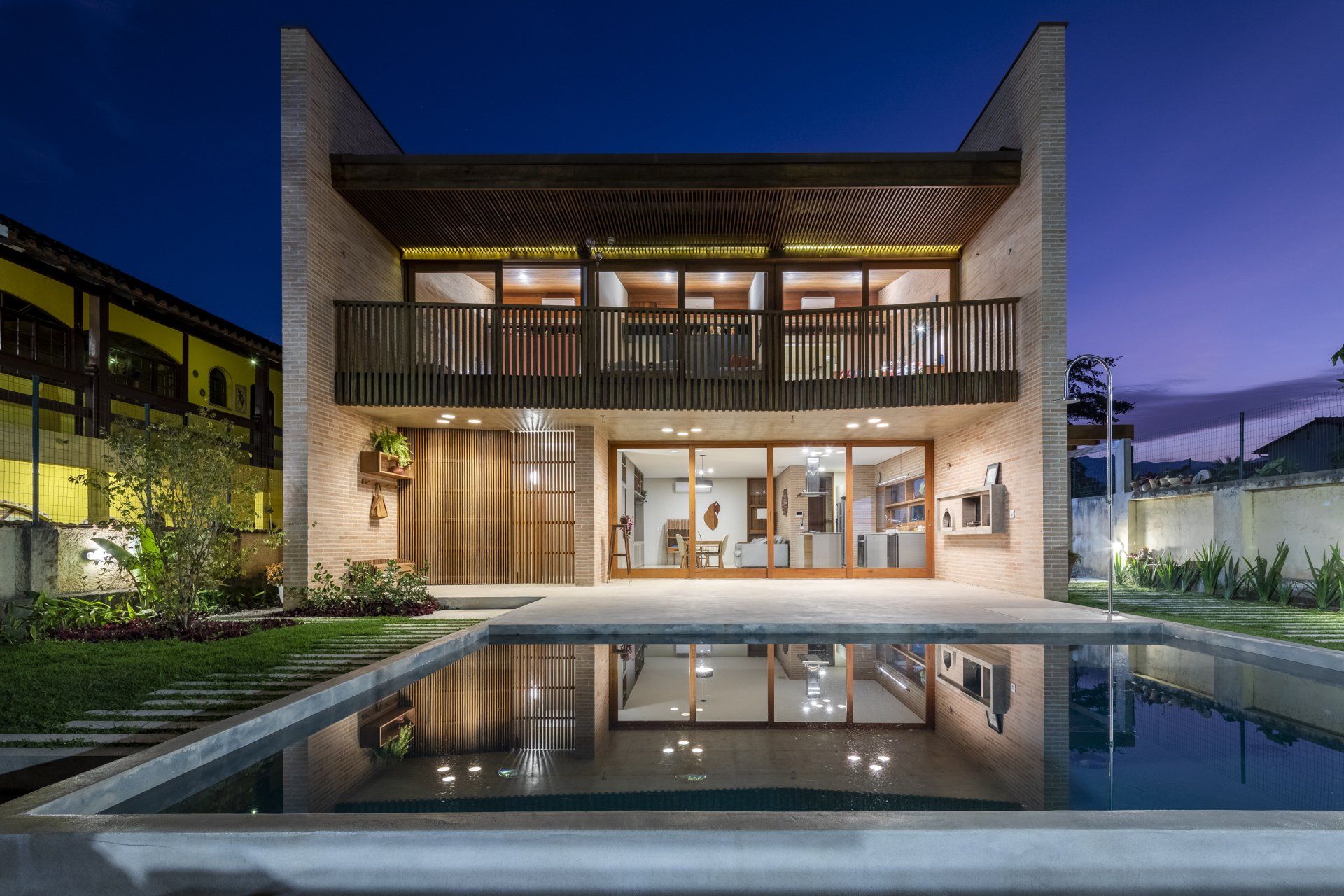 Uma casa grande com piscina em frente à noite.
