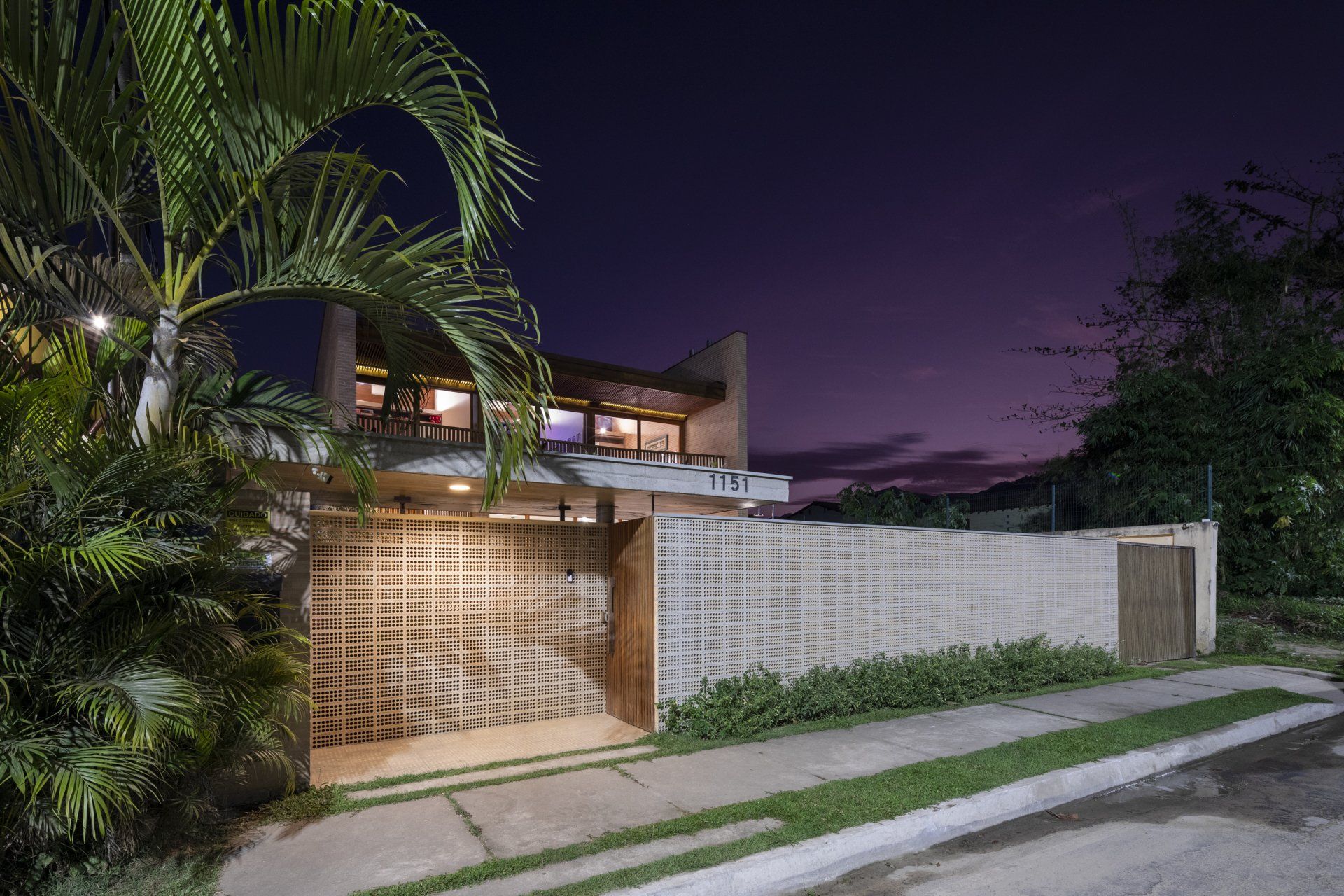 Uma casa é iluminada à noite com uma palmeira na frente.