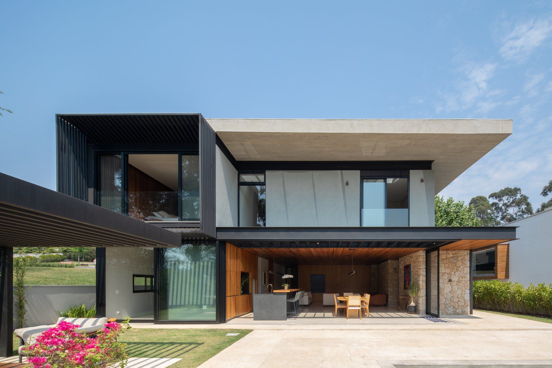 Uma casa moderna com muitas janelas e uma pérgula na frente.