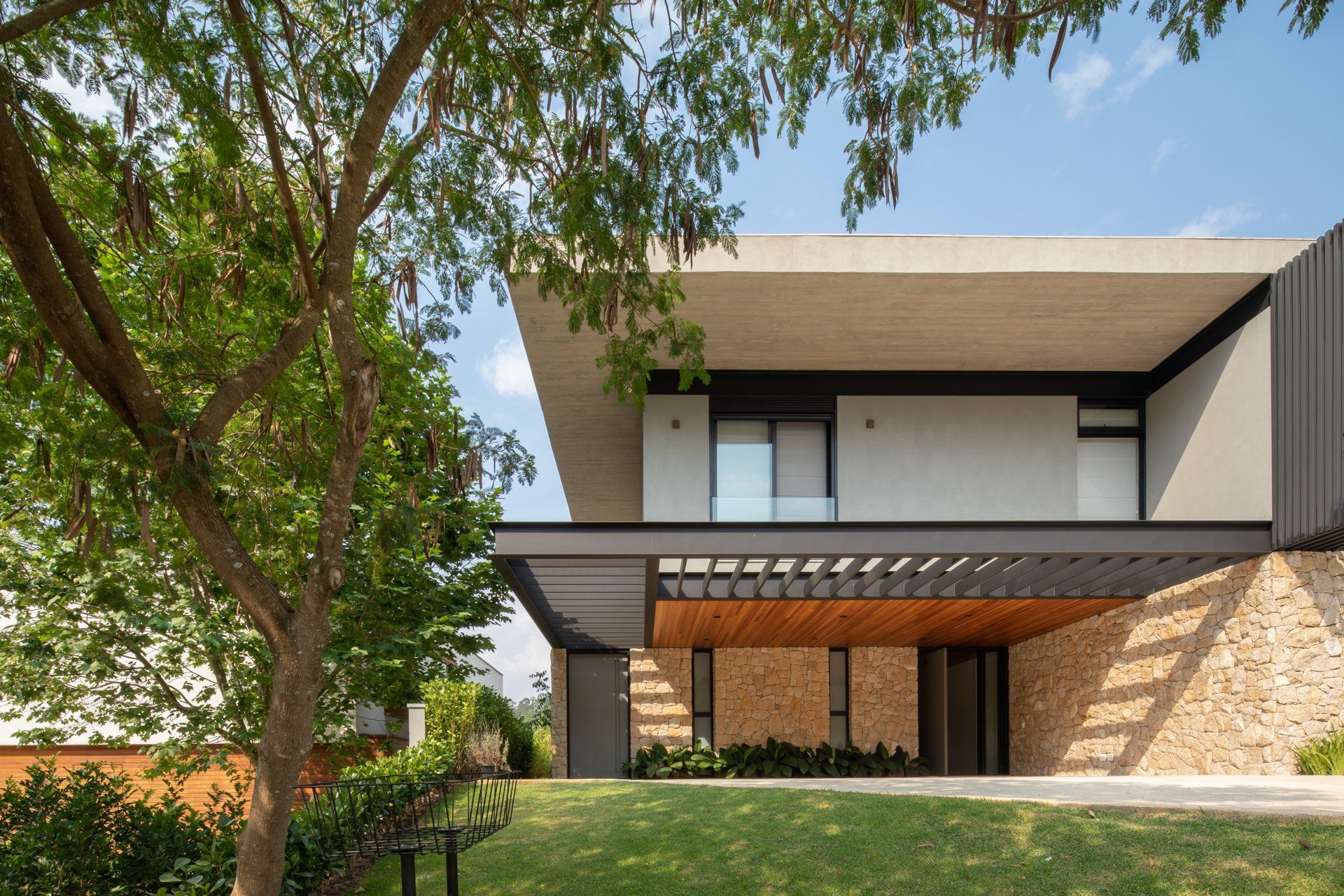Uma casa moderna com pérgula e uma árvore na frente.