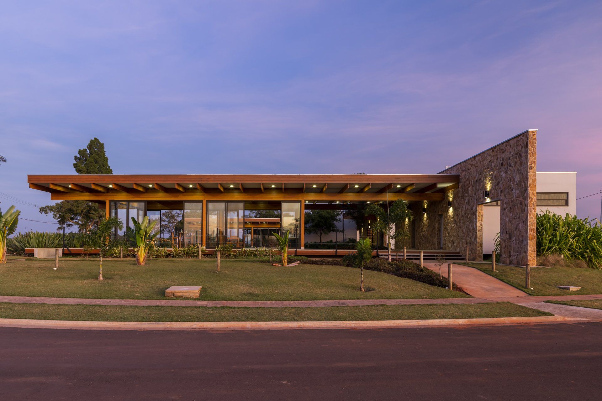 Uma casa moderna com telhado de madeira e parede de pedra está situada no topo de um campo verdejante.