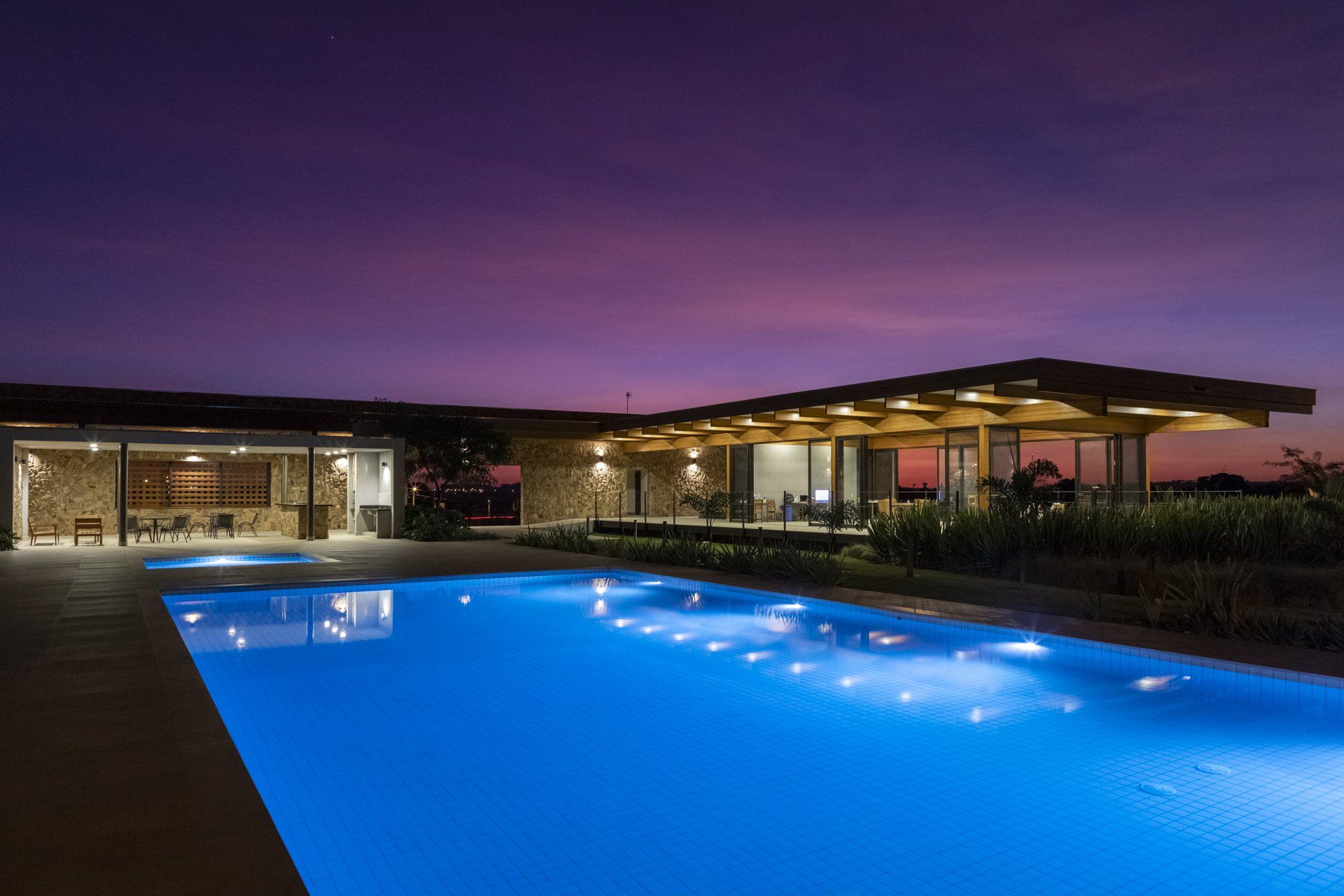 Uma grande piscina fica iluminada à noite em frente a uma casa.