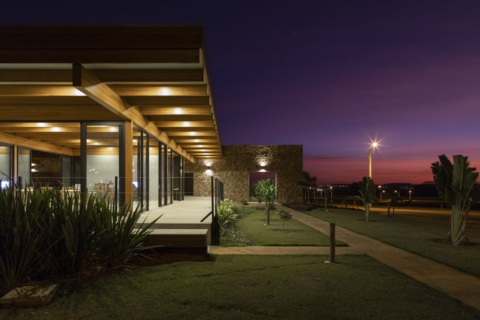 Uma casa grande com muitas janelas fica iluminada à noite.