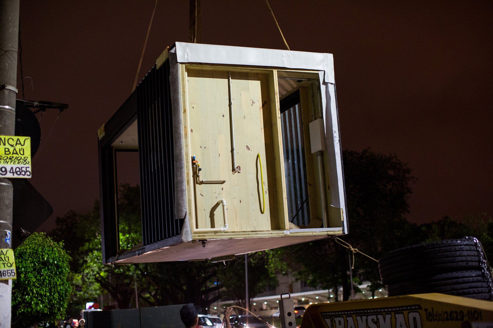 Um grande contêiner está sendo içado por um guindaste à noite.