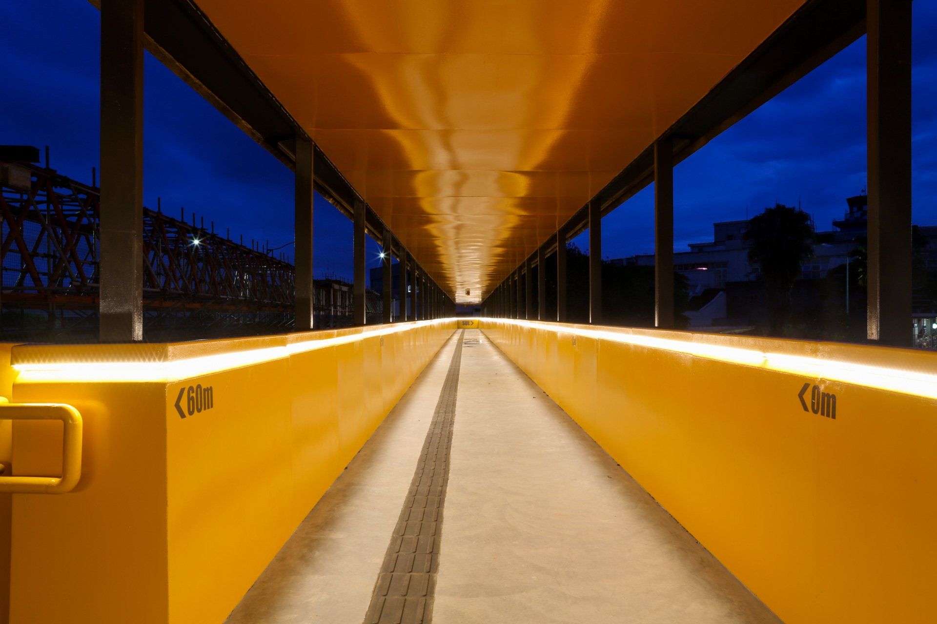 Uma longa passarela amarela com luzes ao lado à noite.