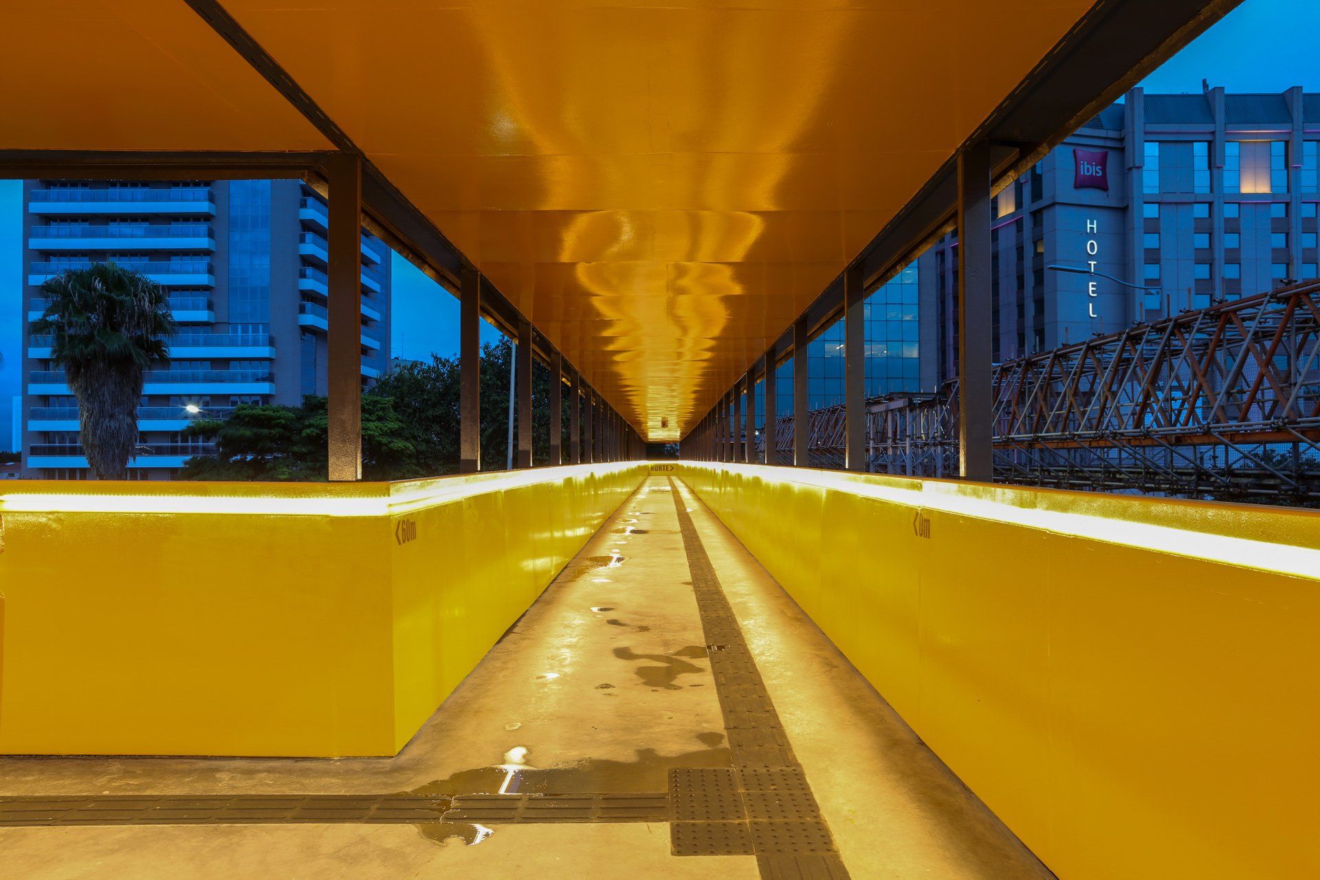 Uma longa passarela amarela que atravessa uma cidade à noite.