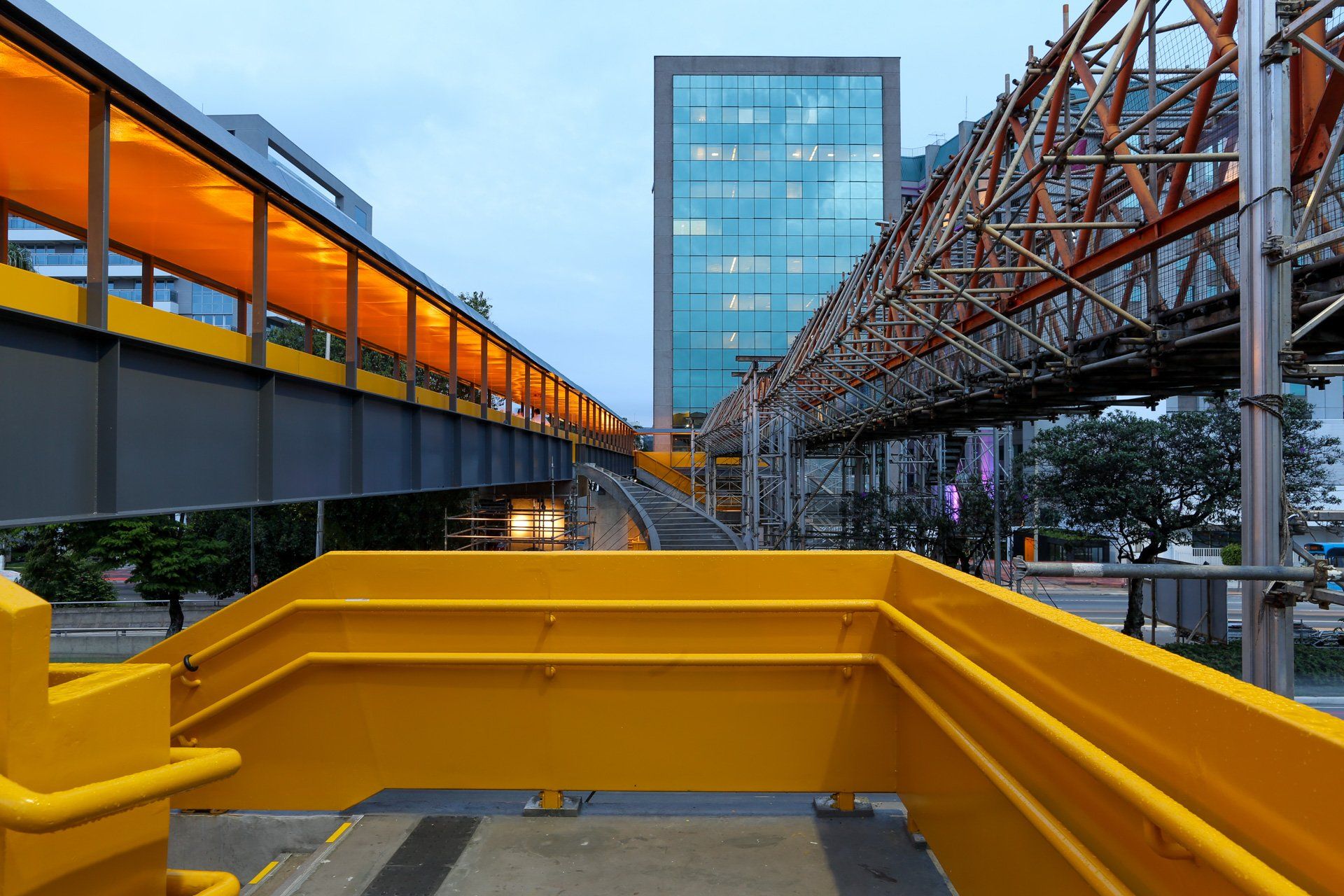 Uma ponte amarela sobre uma rua da cidade com um prédio ao fundo.
