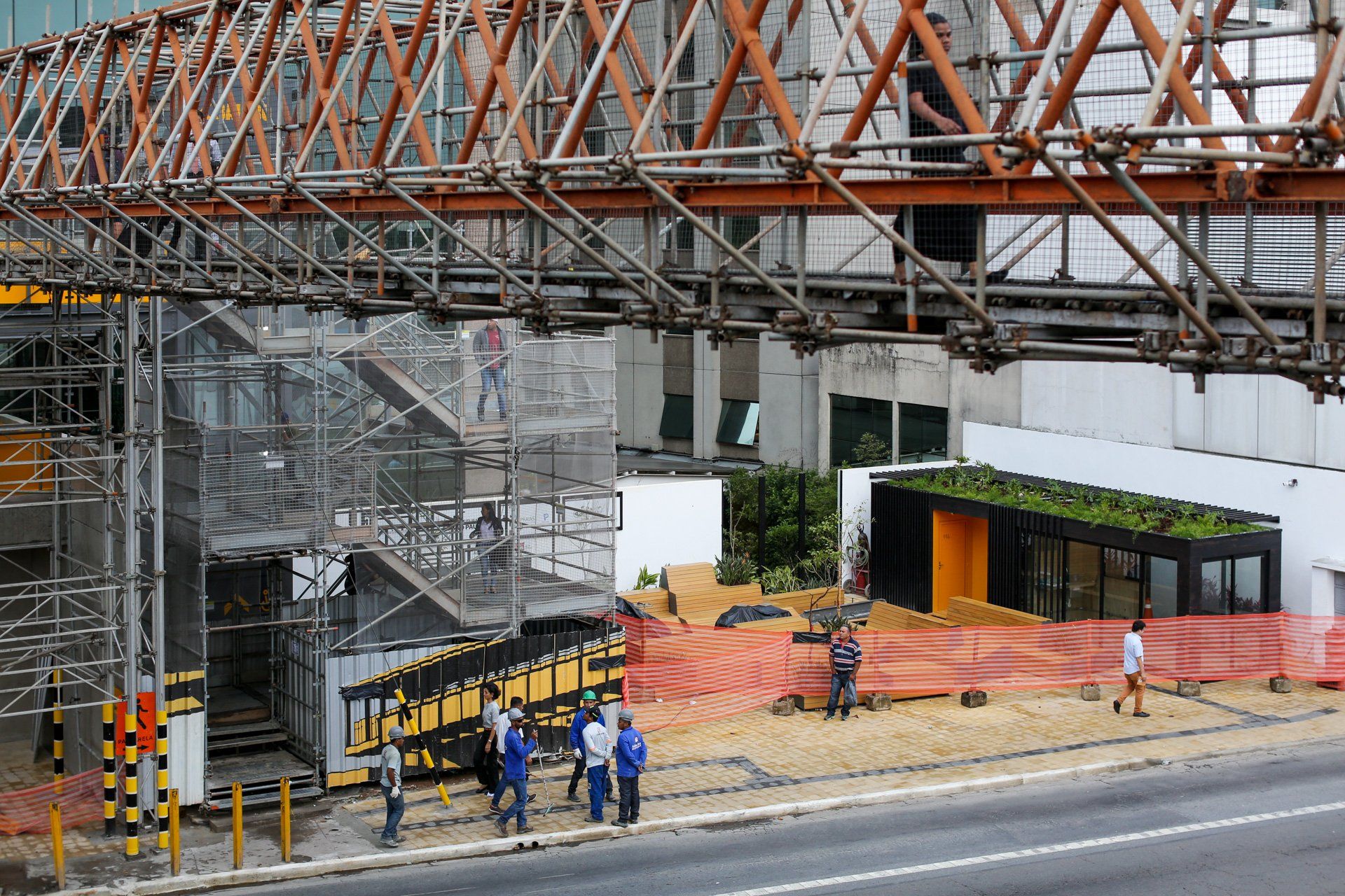 Um grupo de pessoas está parado na beira de uma estrada em frente a um prédio em construção.