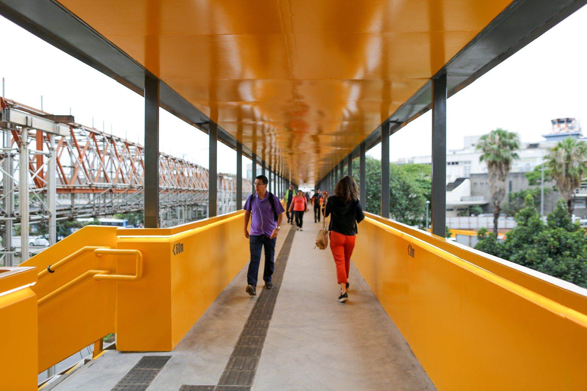 Um grupo de pessoas atravessa uma ponte amarela.