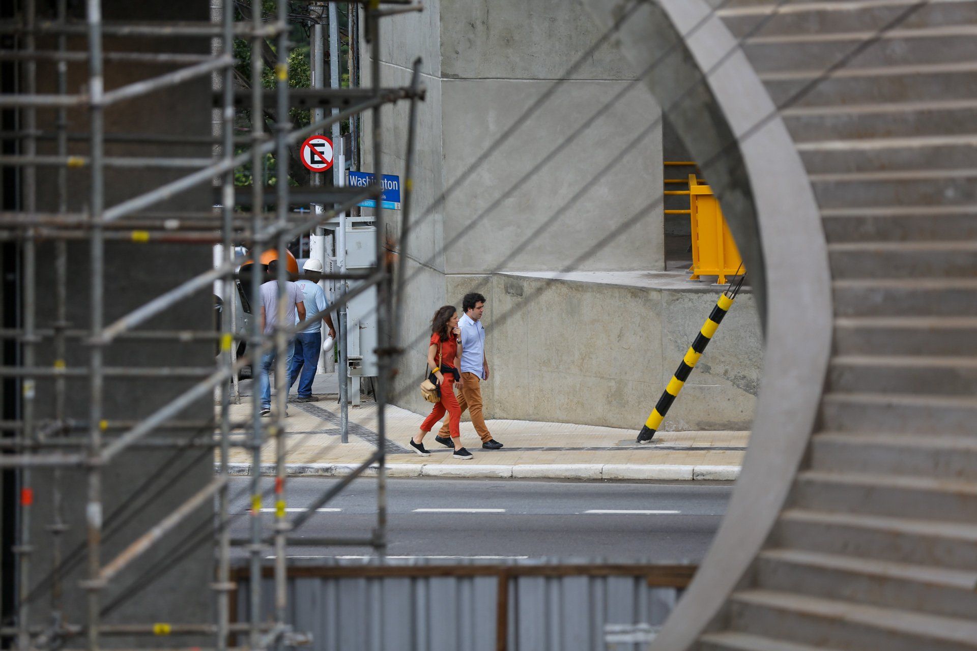 Um grupo de pessoas caminha por uma rua em frente a um prédio em construção.