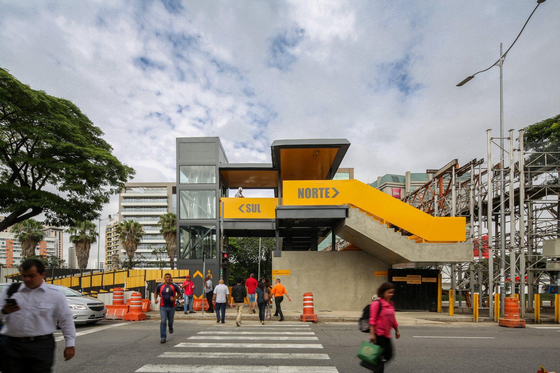 Um grupo de pessoas atravessa uma rua em frente a um prédio amarelo.