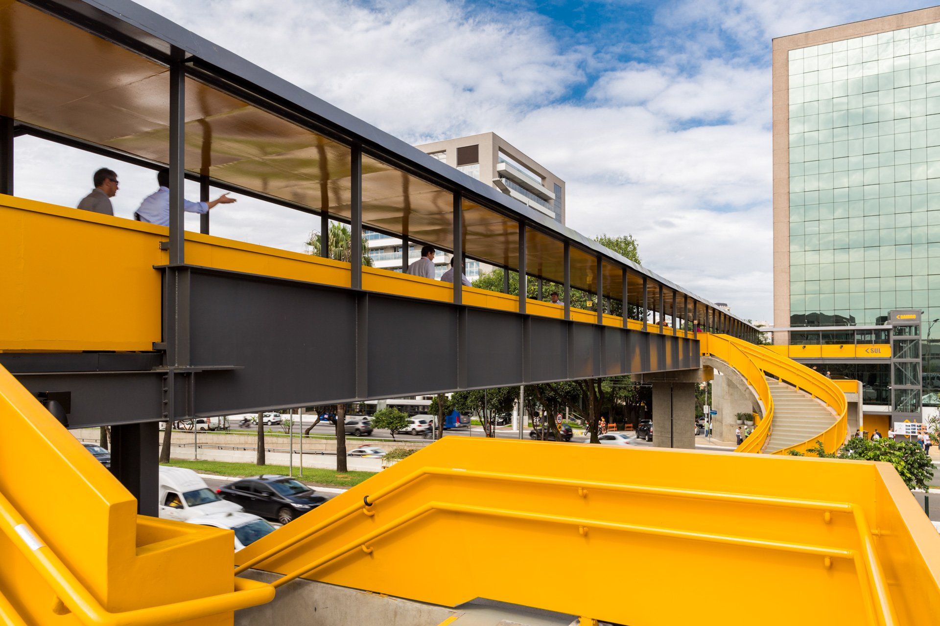 Duas pessoas estão atravessando uma ponte amarela em uma cidade.
