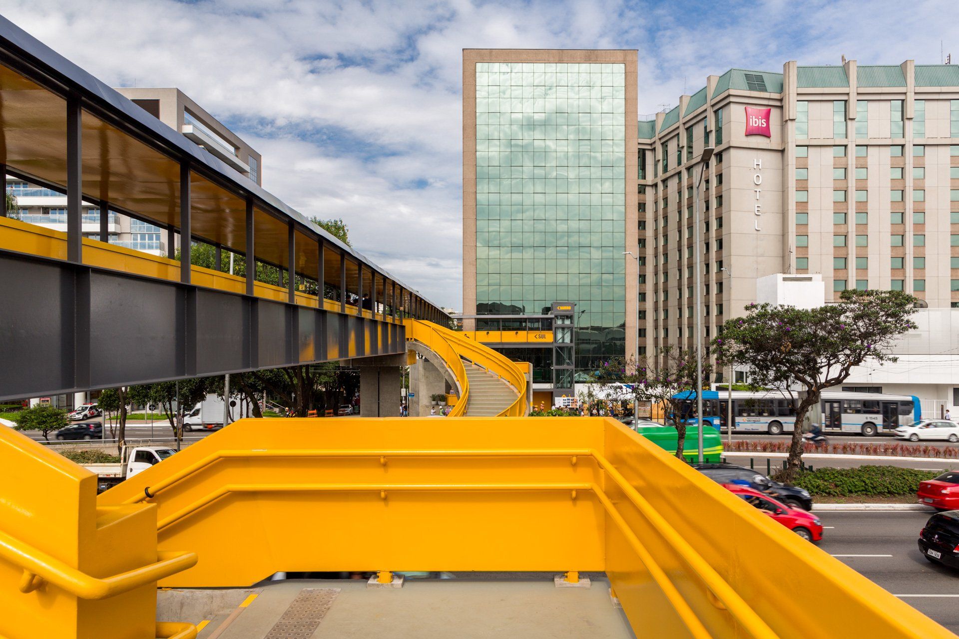 Uma ponte amarela sobre uma rua da cidade com um hotel ao fundo.