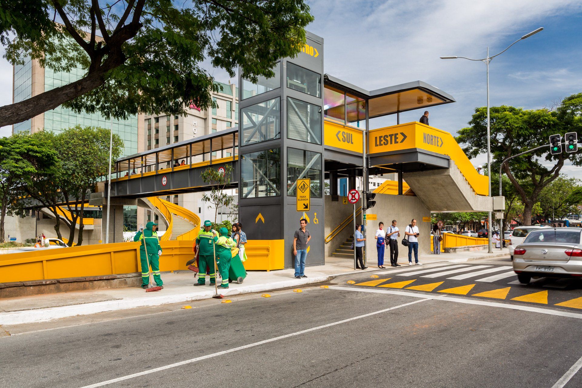 Um grupo de pessoas está parado na calçada em frente a um prédio amarelo.