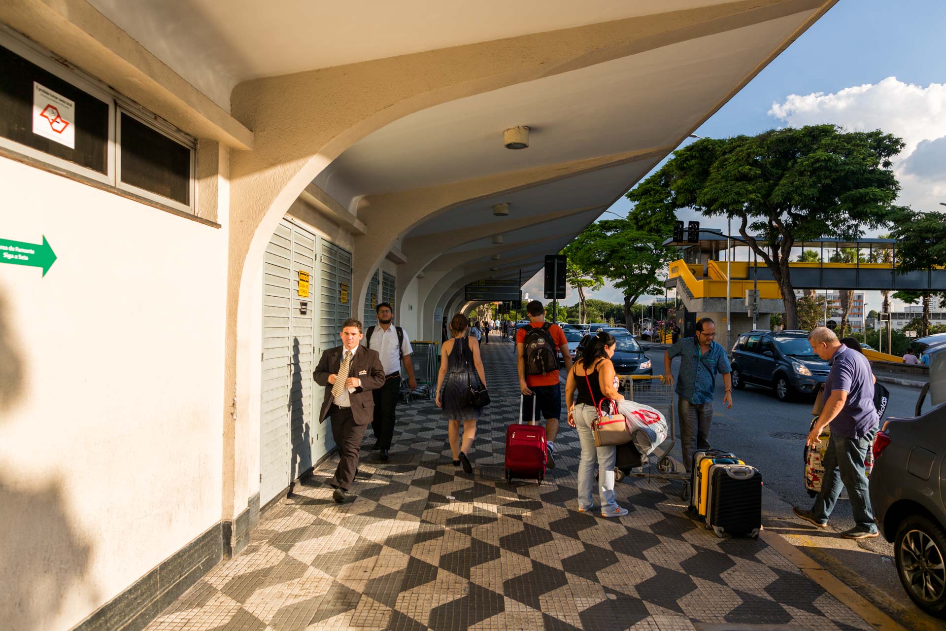 Um grupo de pessoas caminha pela calçada com bagagens.