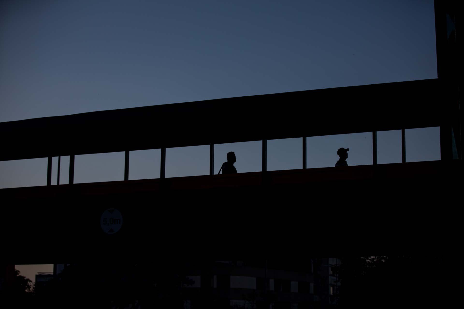 Duas pessoas estão atravessando uma ponte à noite.