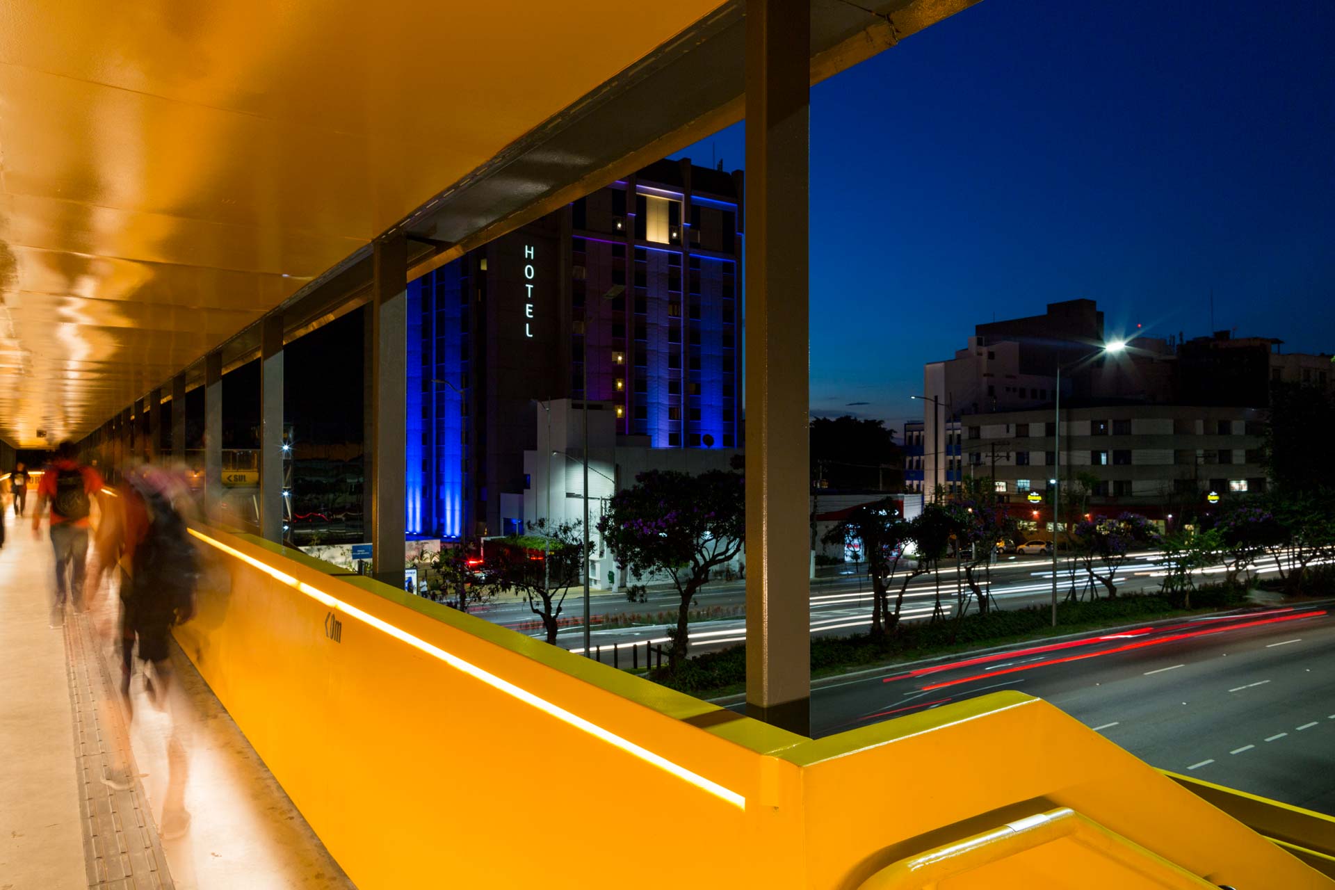 Um grupo de pessoas atravessa uma ponte à noite.