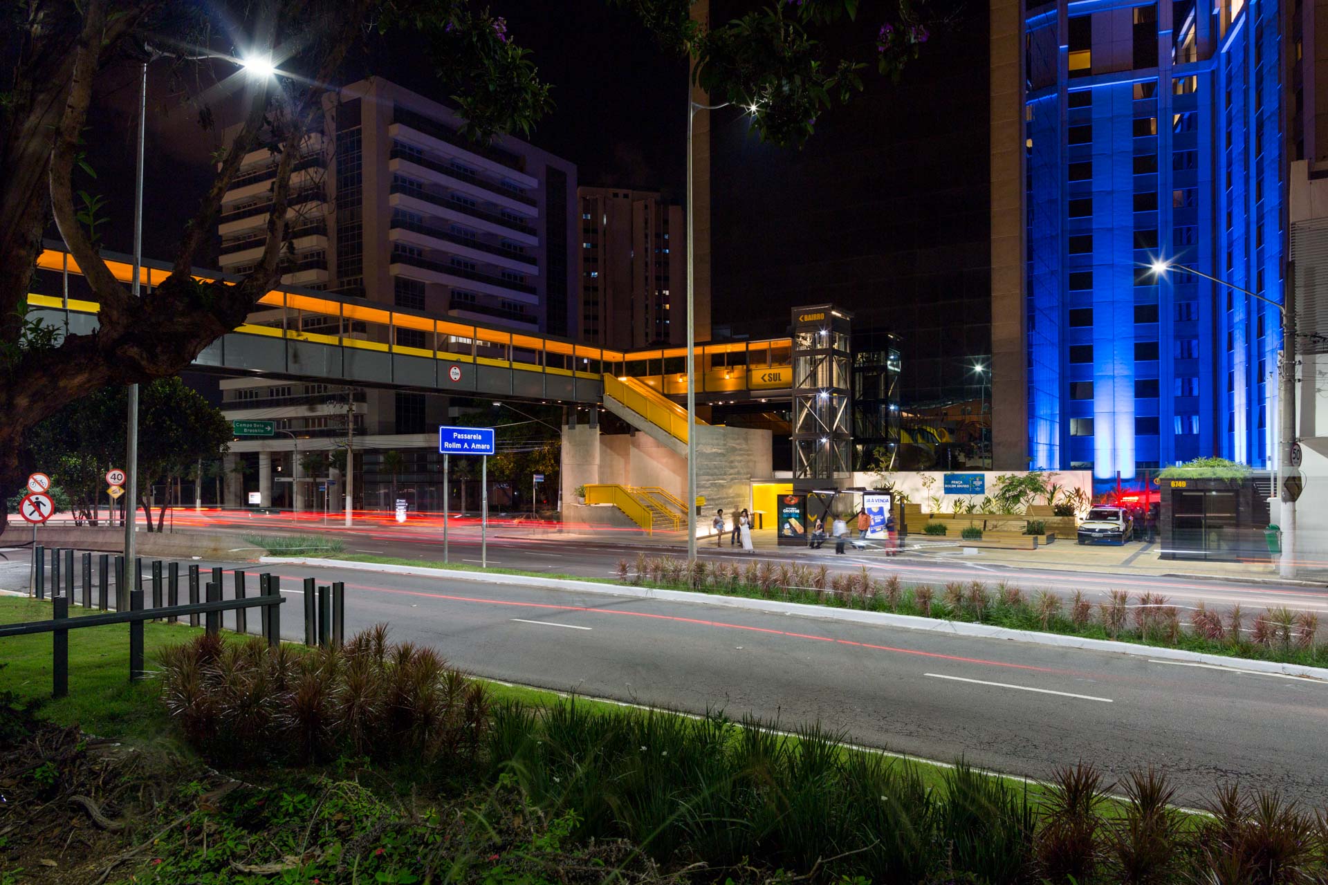 Uma rua da cidade à noite com um prédio azul ao fundo