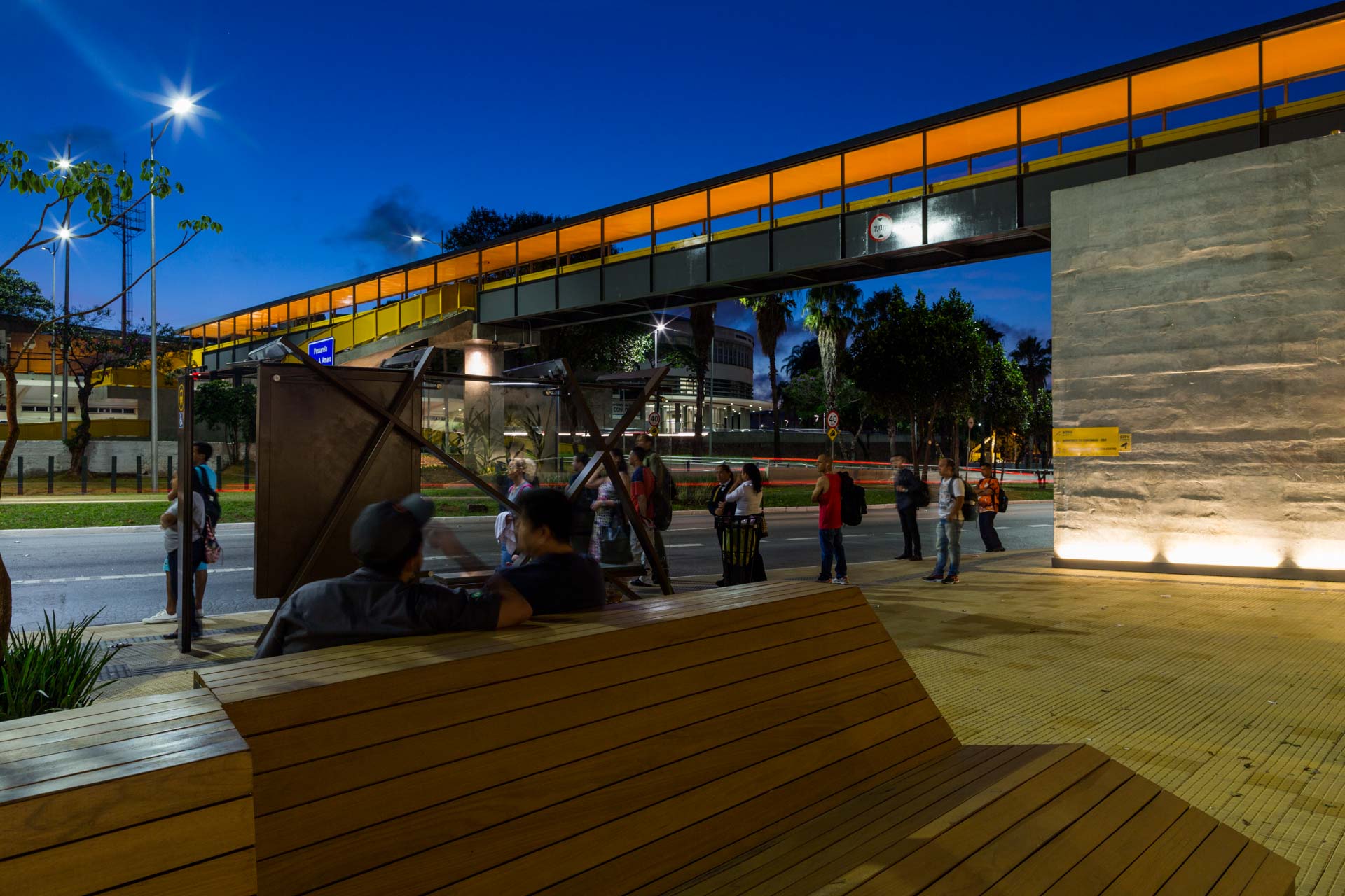 Um grupo de pessoas está sentado em um banco debaixo de uma ponte à noite.