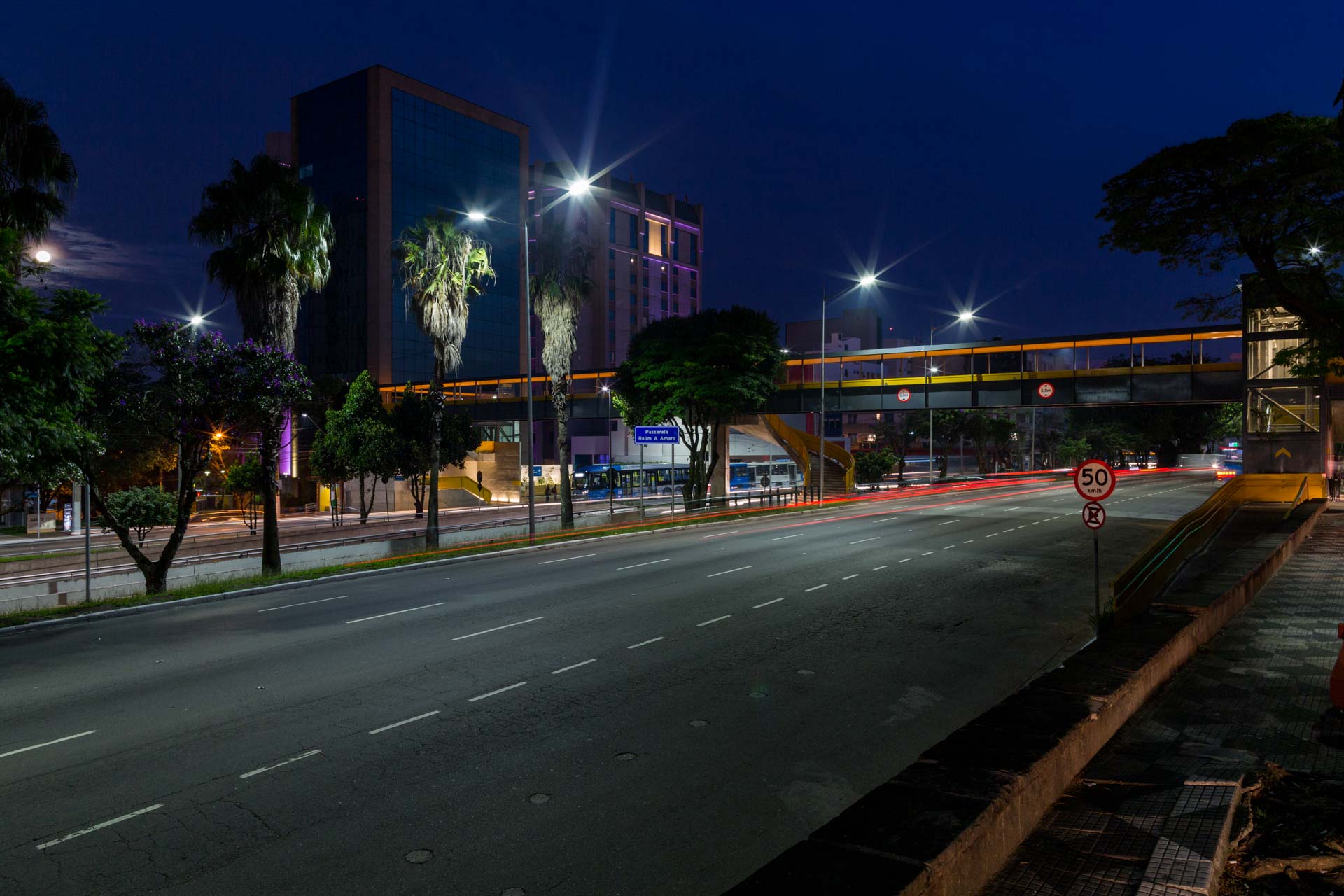Uma rua vazia à noite com uma ponte ao fundo.