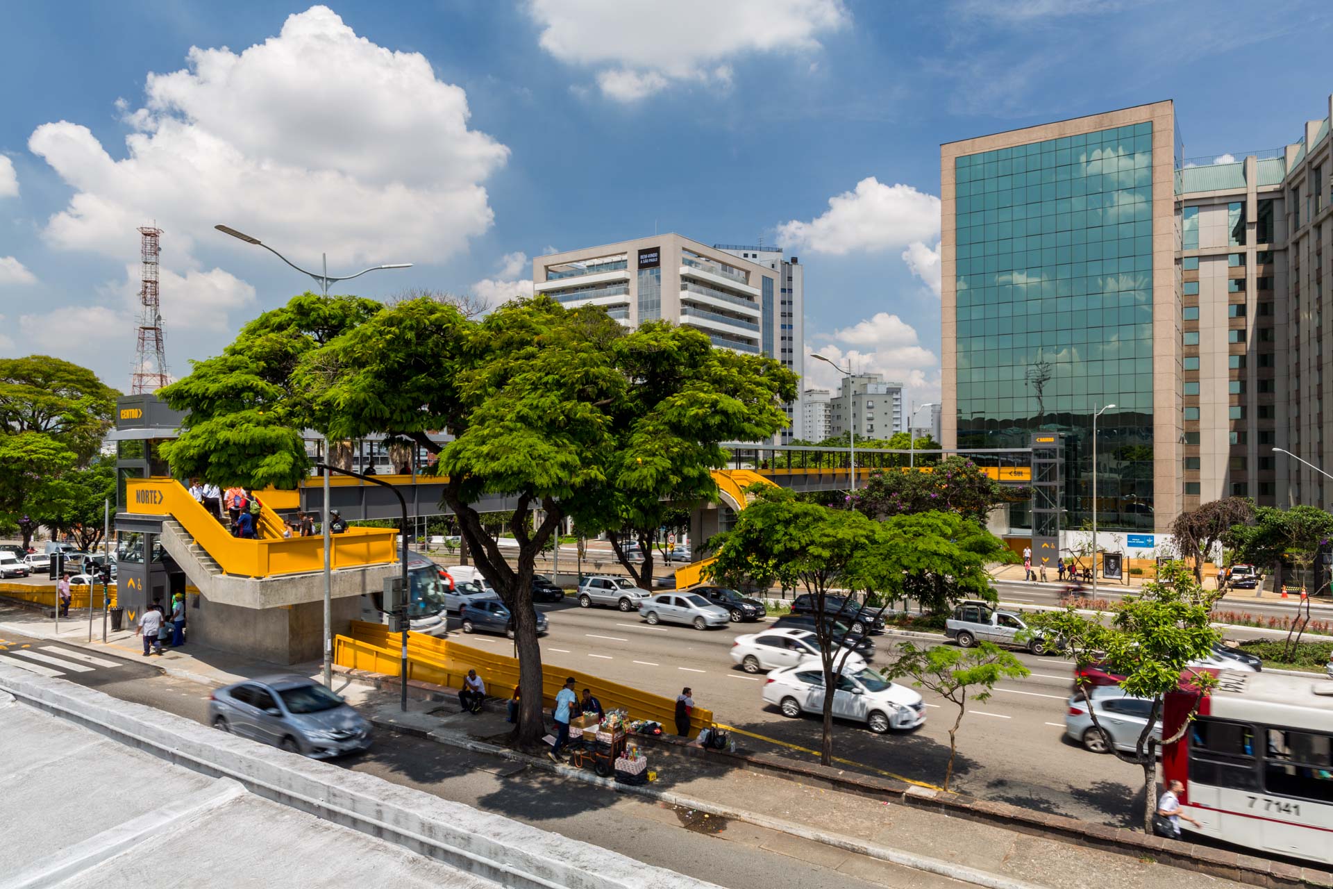Uma vista aérea de uma rua movimentada da cidade com árvores e edifícios ao fundo.