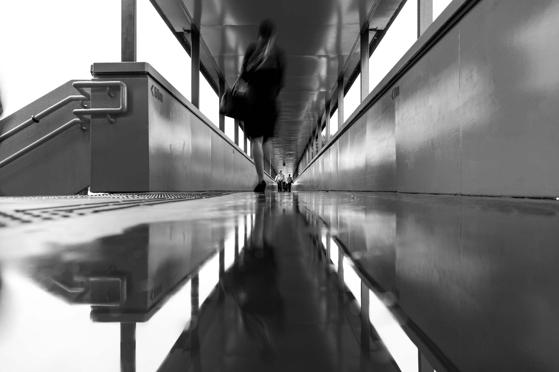 Uma foto em preto e branco de uma pessoa andando em uma ponte