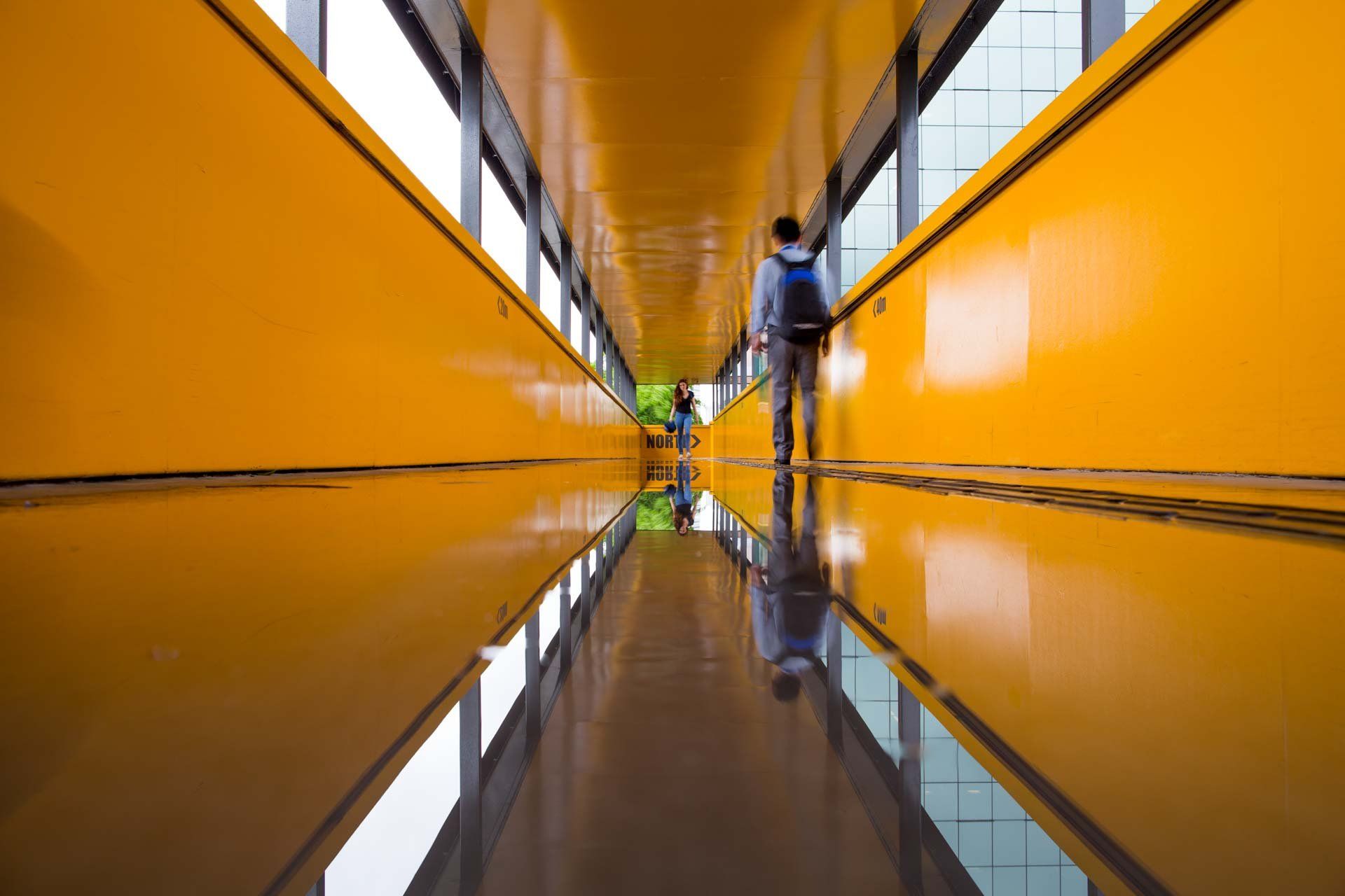 Um homem caminha por um longo corredor amarelo.