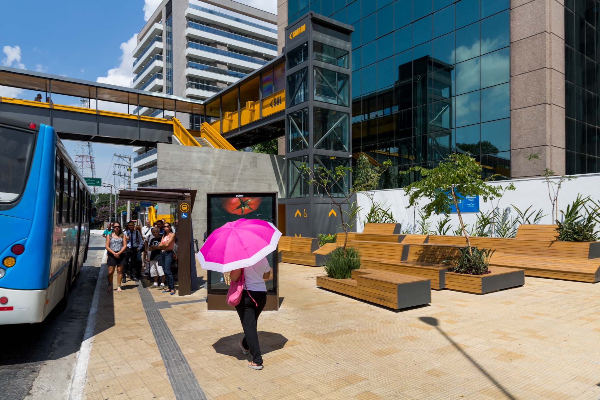 Uma mulher com um guarda-chuva rosa caminha em direção a um ponto de ônibus.