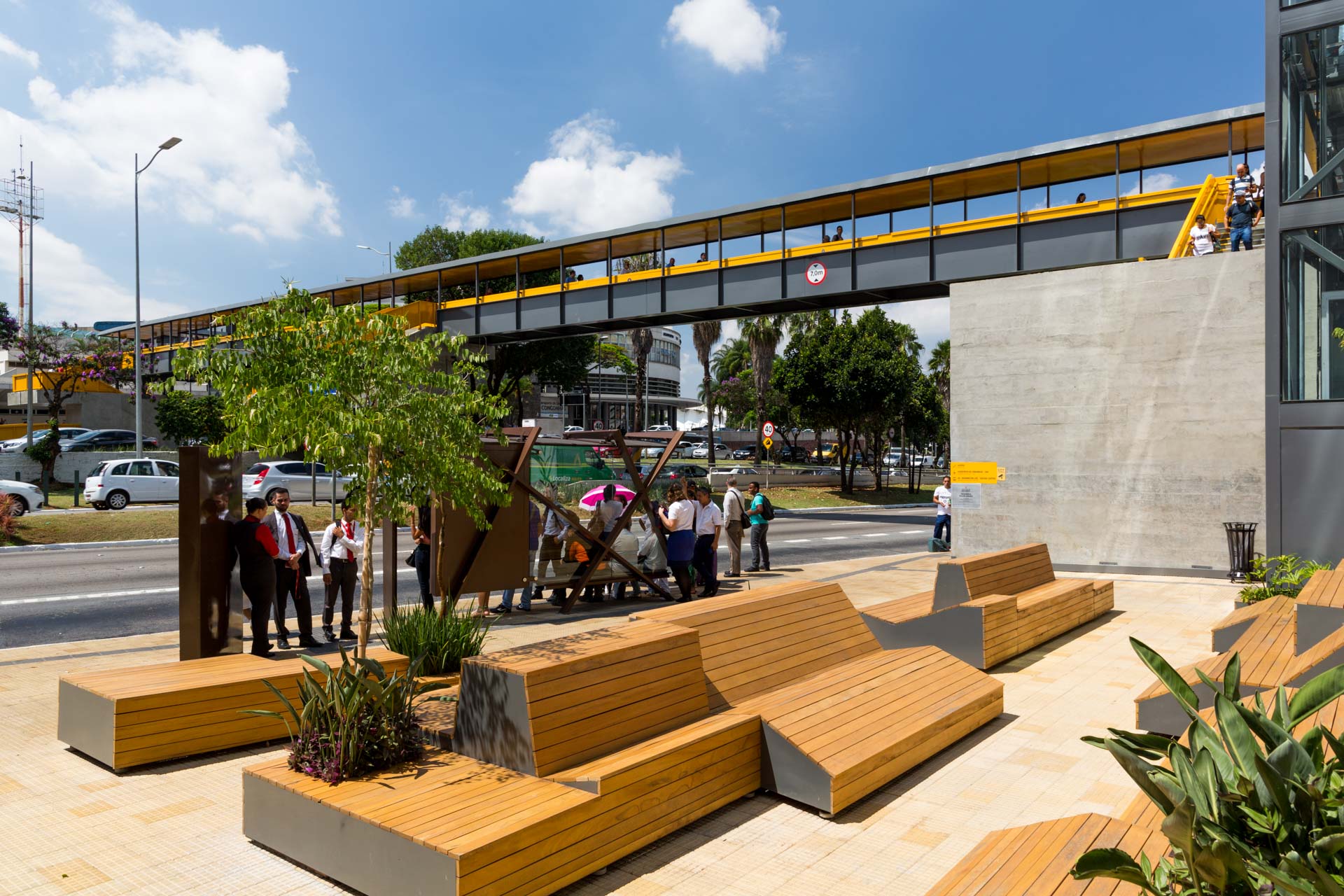 Um grupo de pessoas está sentado em bancos de madeira debaixo de uma ponte.