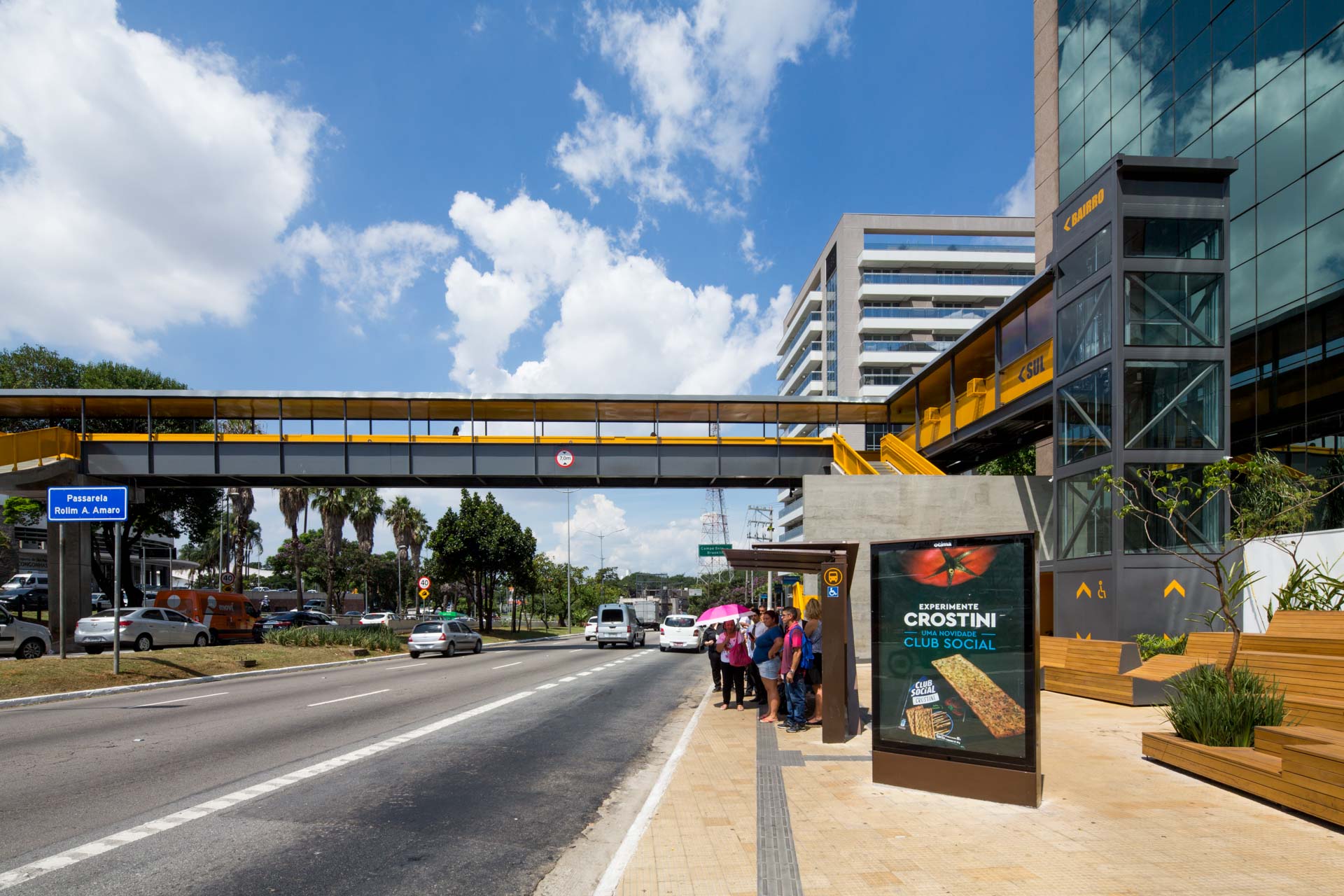 Um grupo de pessoas espera em um ponto de ônibus à beira da estrada.