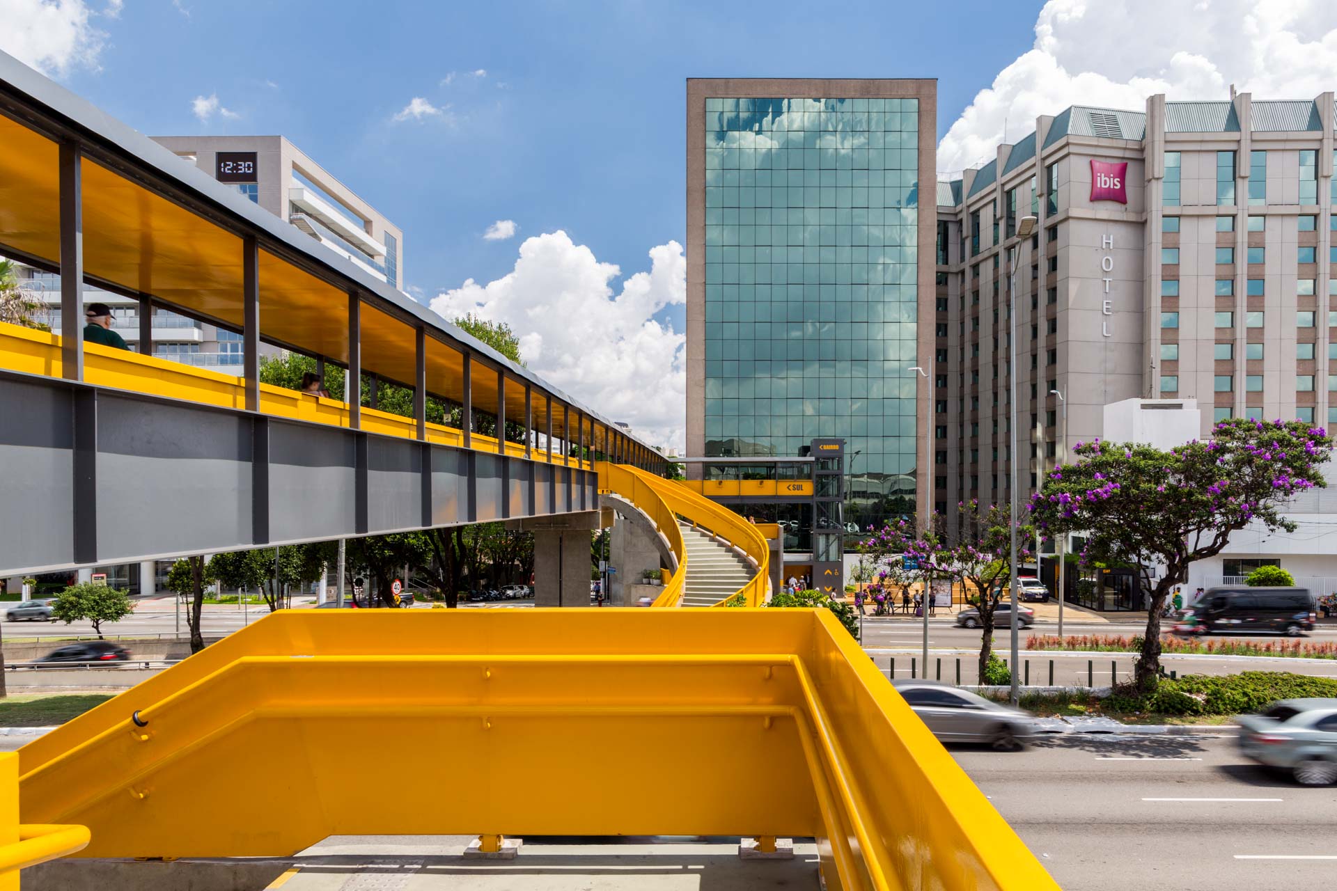 Uma ponte amarela sobre uma rua da cidade com um prédio ao fundo.