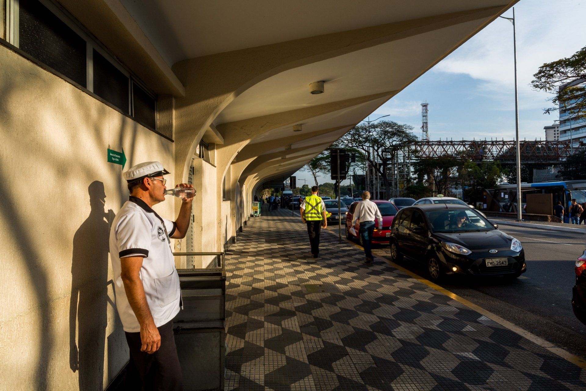 Um homem está bebendo água de uma garrafa enquanto está na calçada.