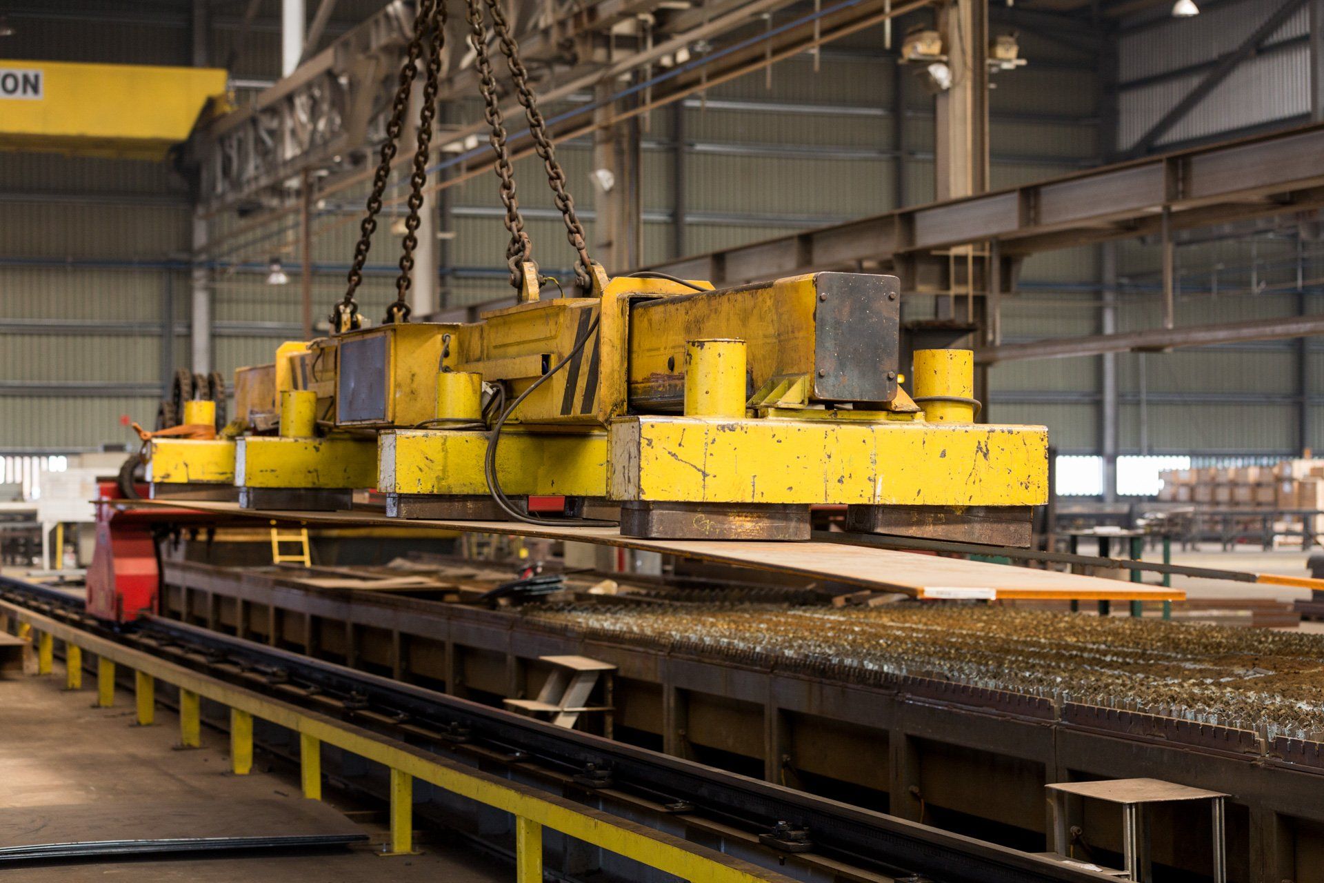 Uma grande máquina amarela está levantando um grande pedaço de metal em uma fábrica.