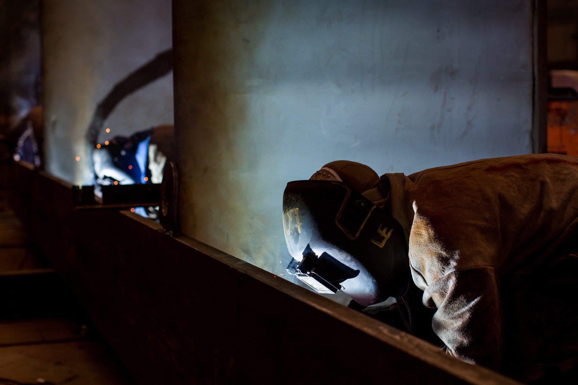 Um homem está soldando um pedaço de metal em um quarto escuro.