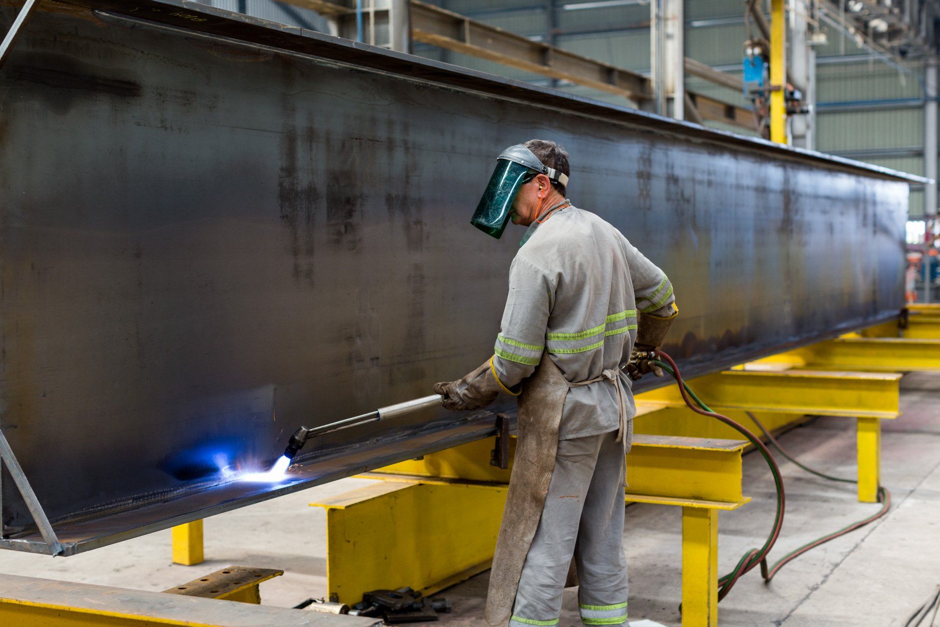Um homem está soldando um grande pedaço de metal em uma fábrica.