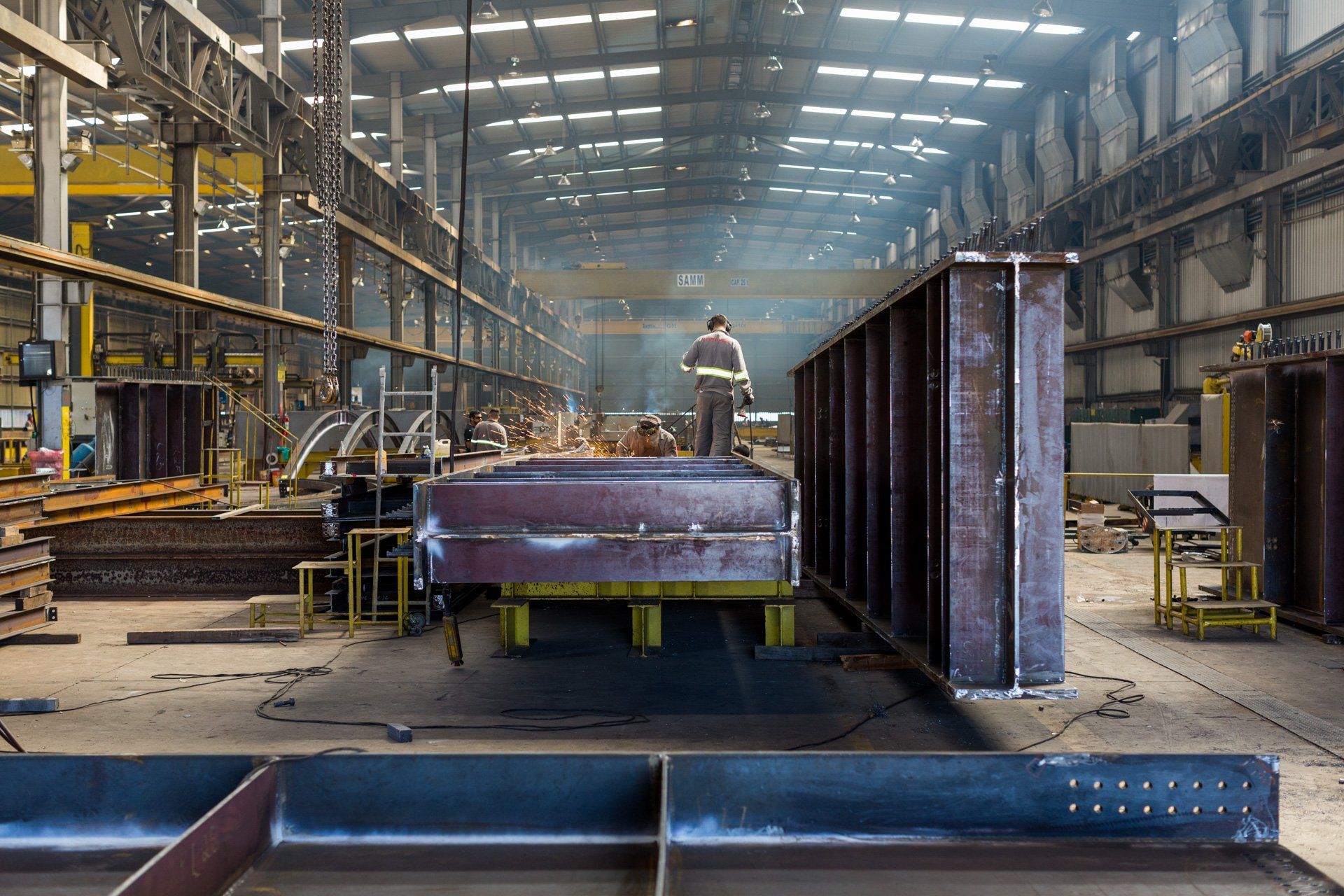 Um homem está em cima de uma grande estrutura metálica em uma fábrica.
