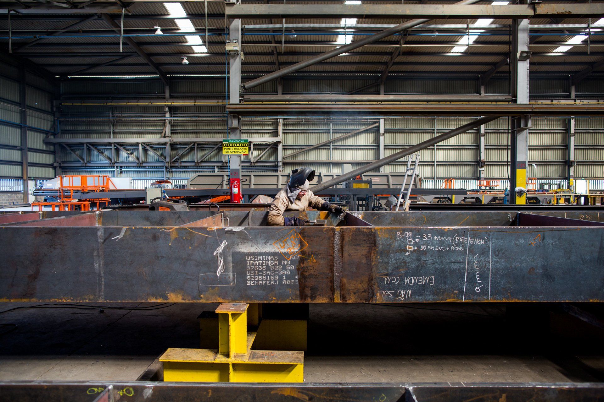 Um homem está soldando um grande pedaço de metal em uma fábrica.