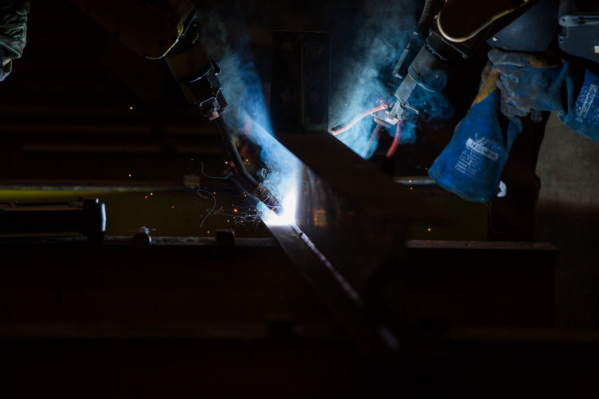 Um homem está soldando um pedaço de metal em um quarto escuro.