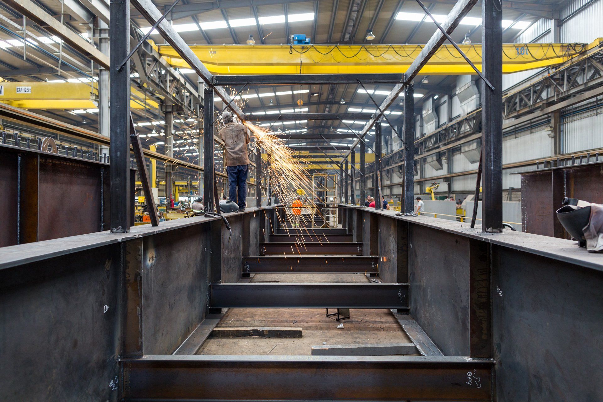 Um homem está soldando uma estrutura metálica em uma fábrica.