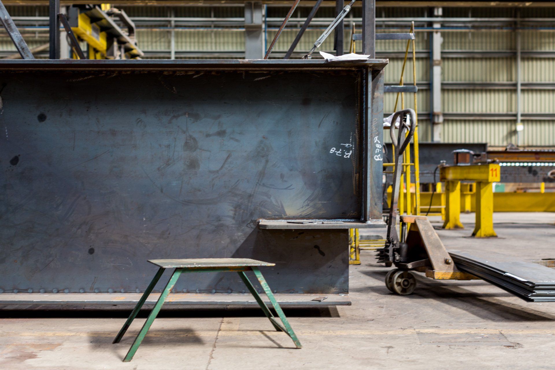 Uma mesa de piquenique está em frente a uma grande estrutura metálica em uma fábrica.