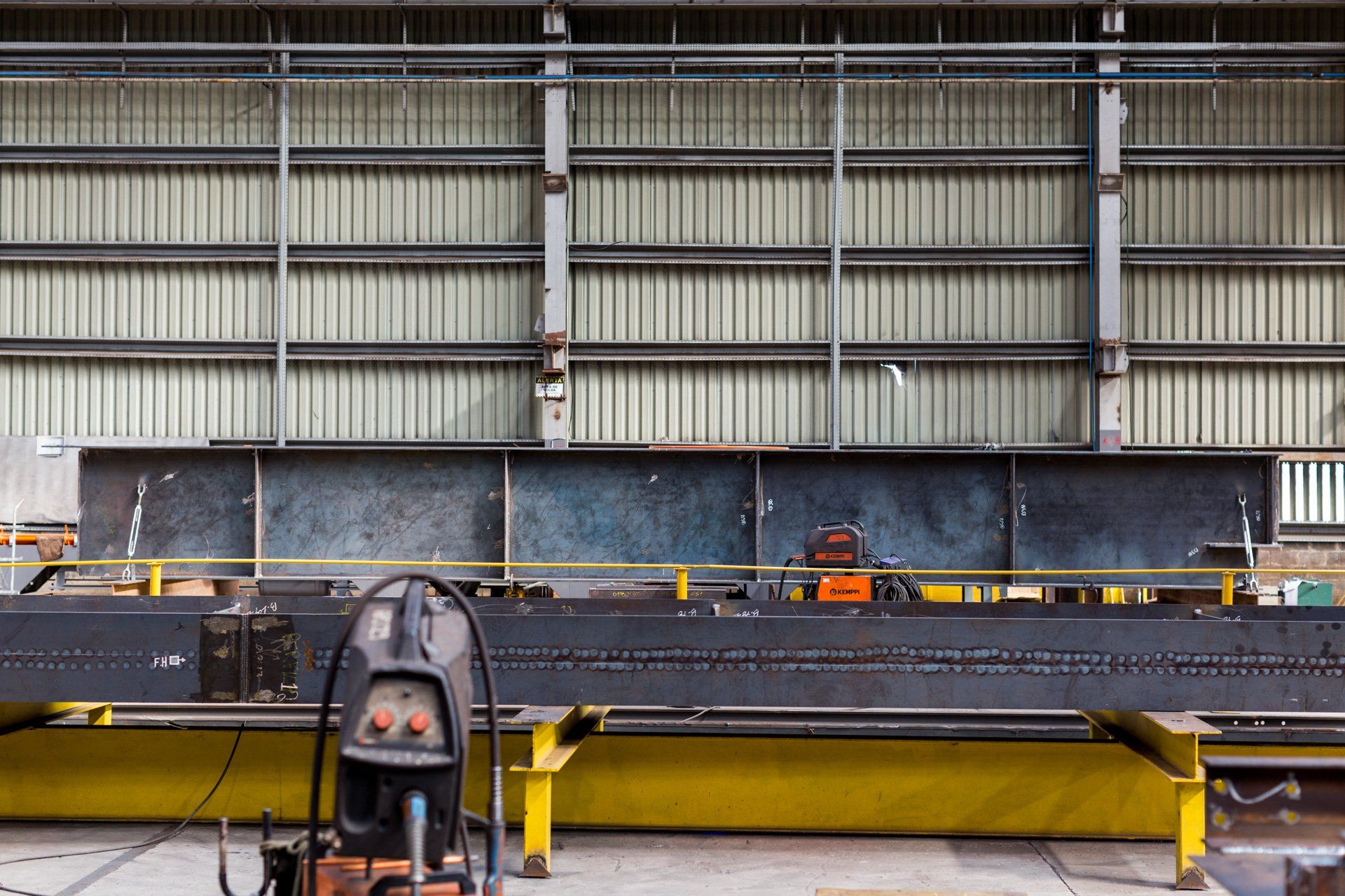 Um aspirador de pó está em frente a uma grande estrutura metálica em uma fábrica.
