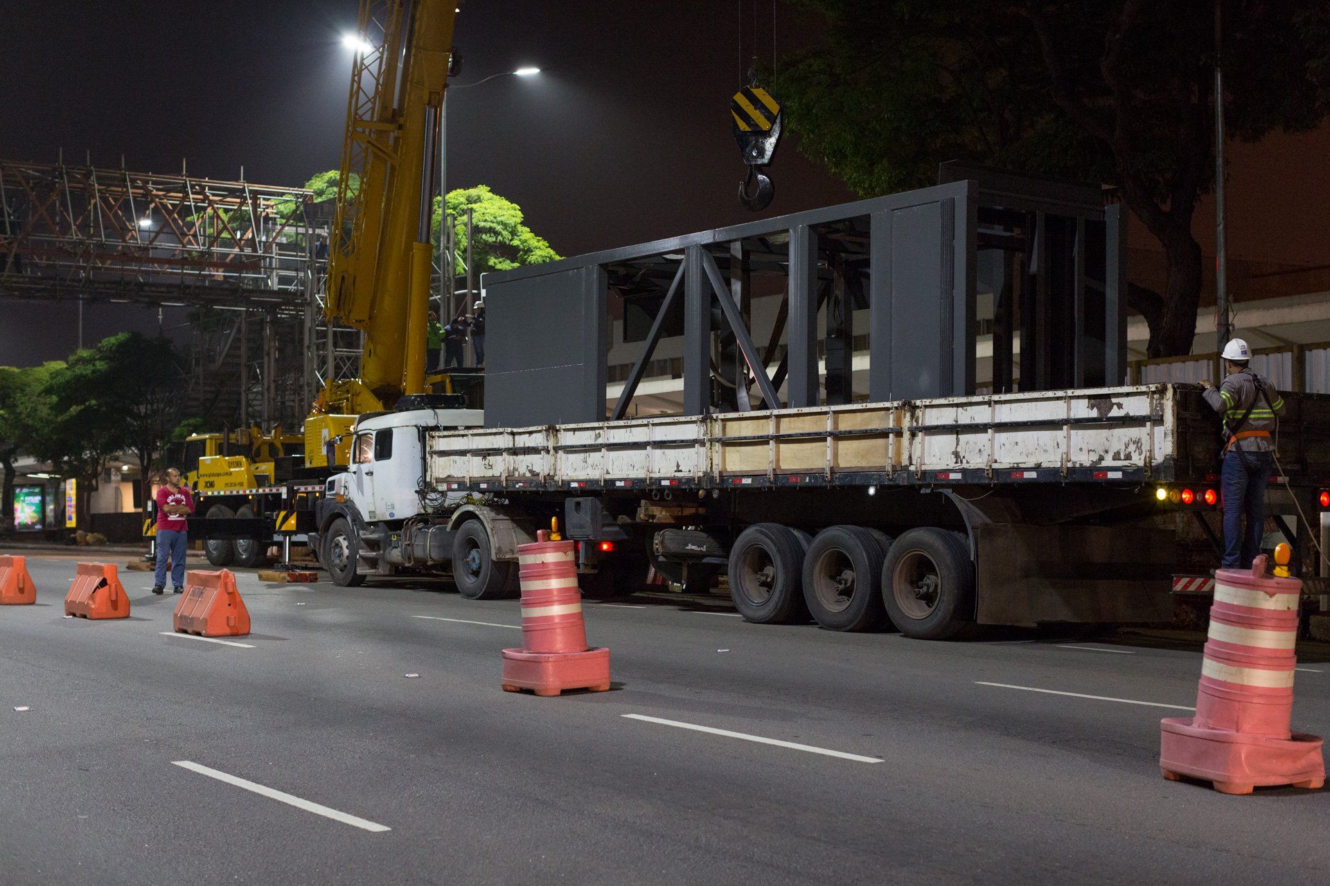 Um caminhão está passando por uma rua à noite com um guindaste ao fundo.